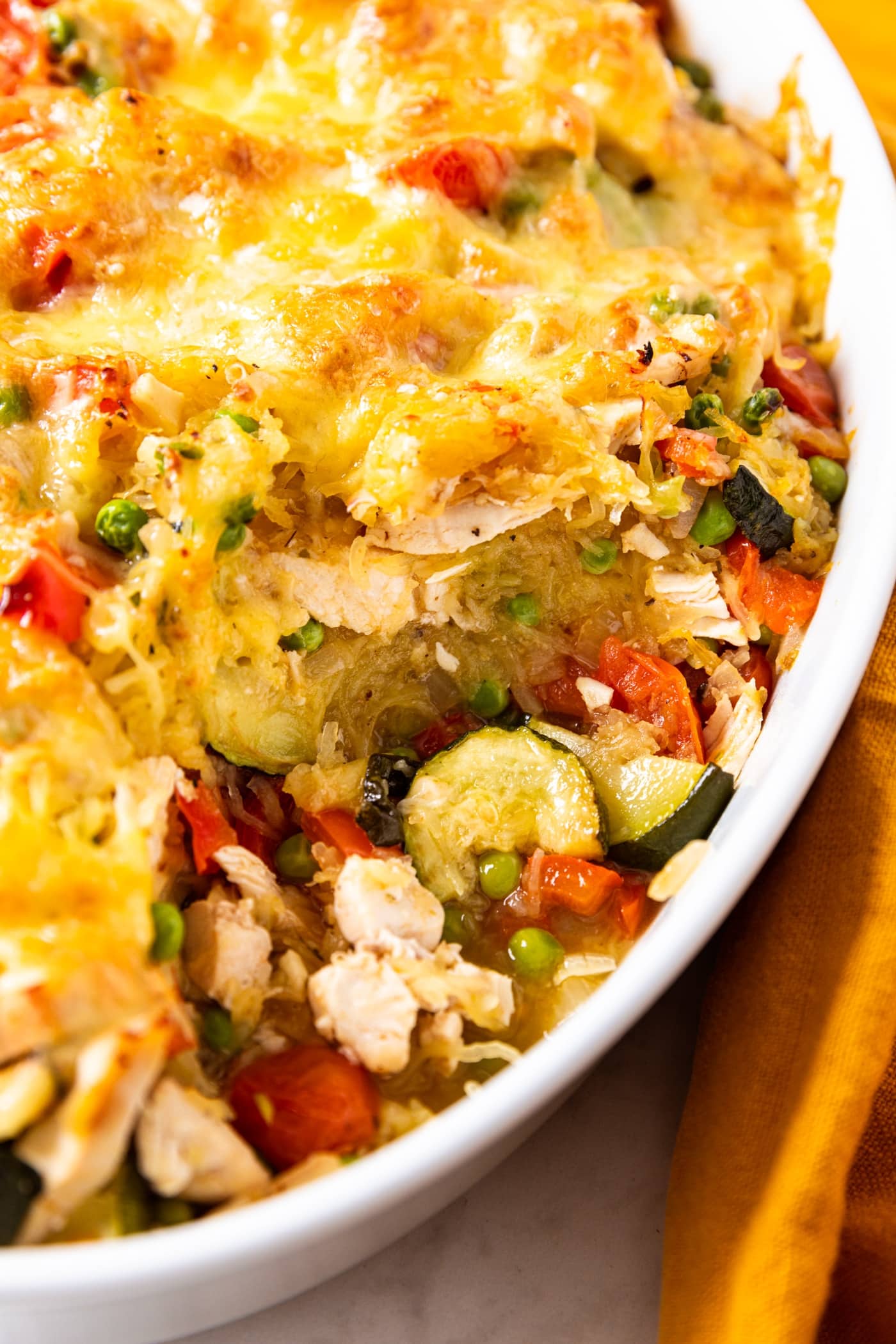 White oval baking dish filled with baked spaghetti squash chicken casserole with vegetables sitting in space from spoonful removed.