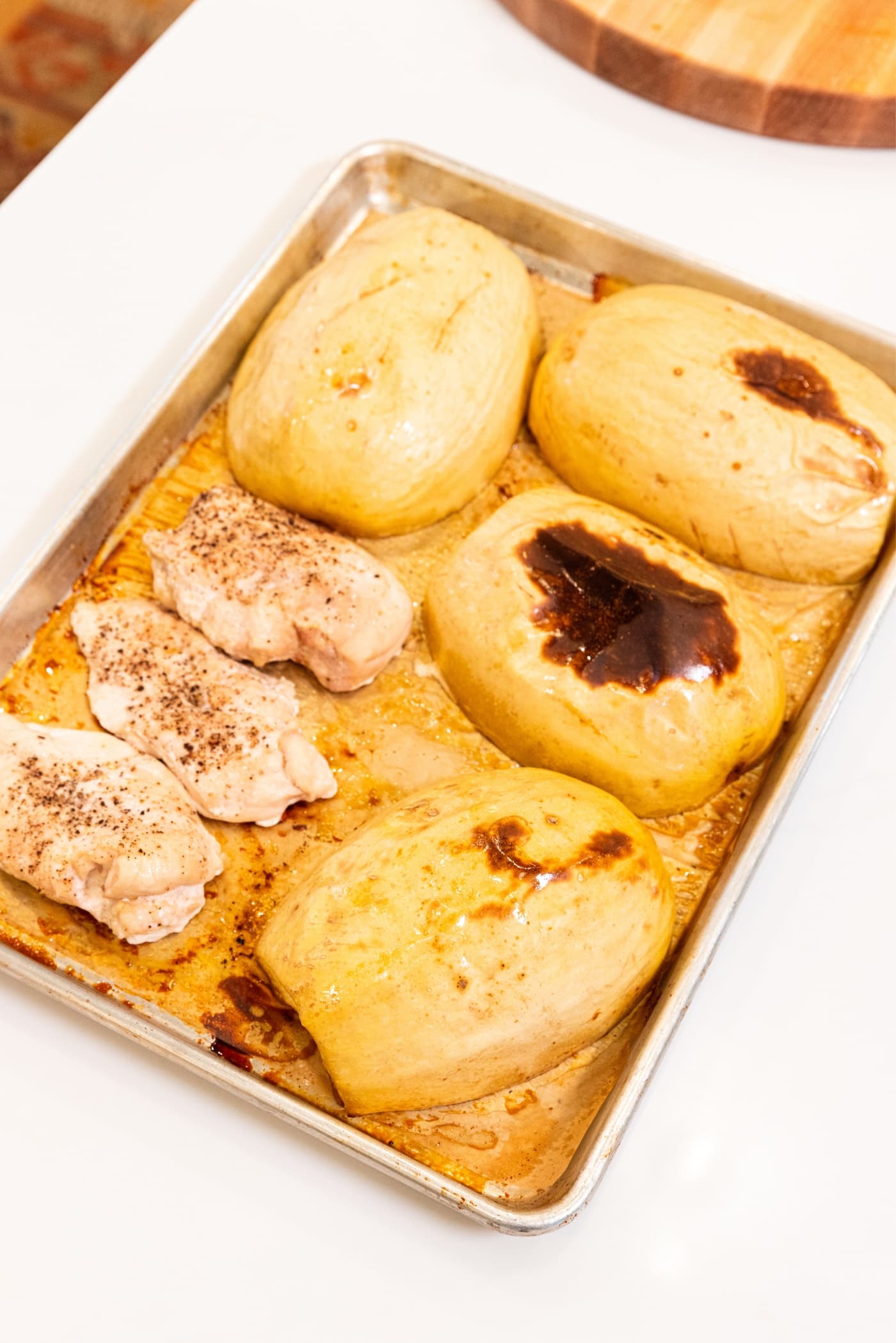 Parchment-lined baking sheet with roasted pieces of squash and chicken breasts with a few brown spots on top of the squash sitting on white countertop after coming out of the oven.