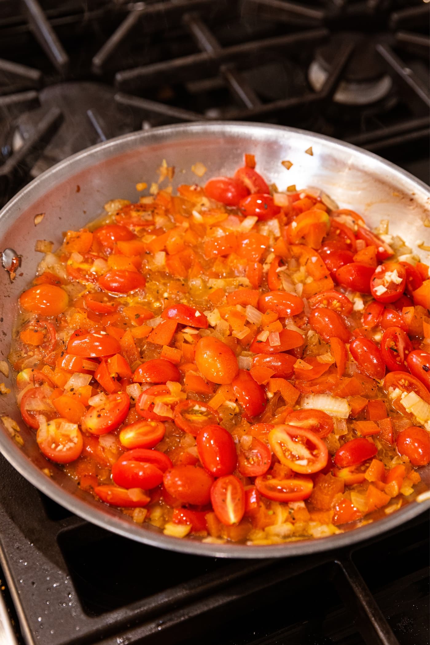 Simmer mixture of halved tomatoes with red bell pepper and onion in skillet on stovetop.