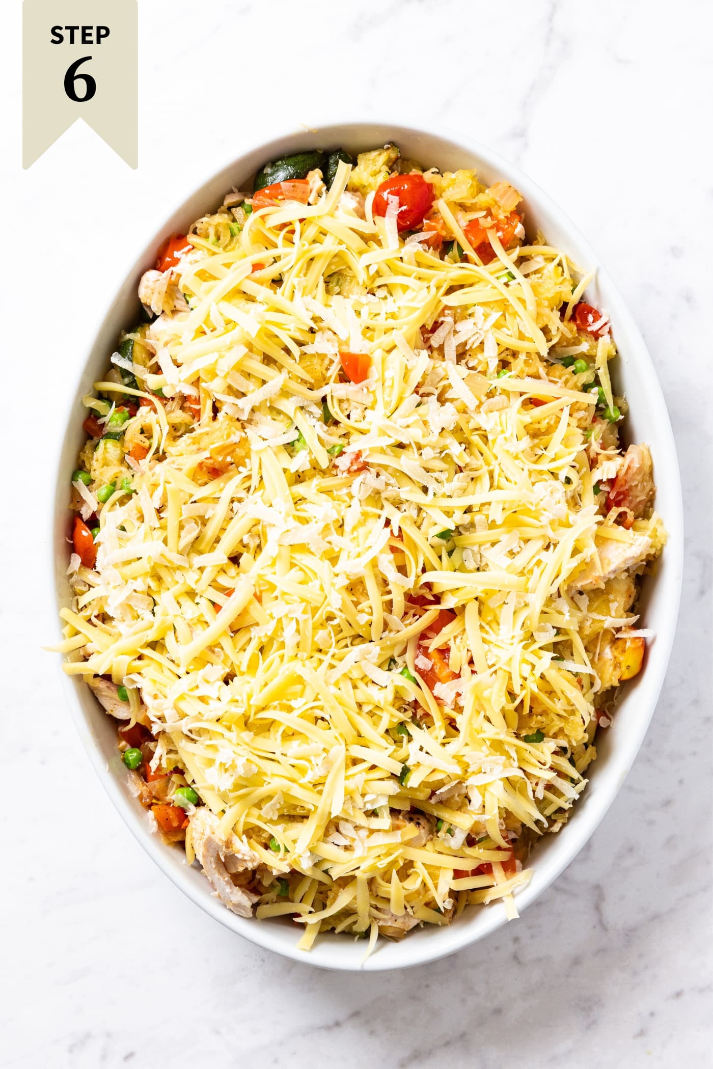 Oval white baking dish filled with unbaked spaghetti squash chicken casserole with tomatoes showing through and topped with unmelted mozzarella cheese right before going into the oven to bake.