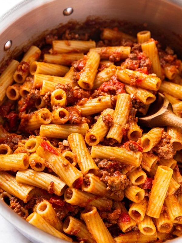Metal stockpot sitting on marble surface with pasta covered in bolognese sauce with wooden spoon resting in pot.