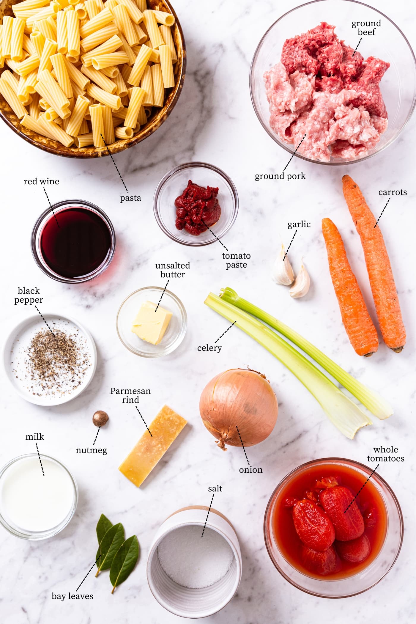 White marble surface filled with all ingredients needed to make bolognese including pasta, beef, pork, red wine, tomato sauce, celery, carrots, and more.
