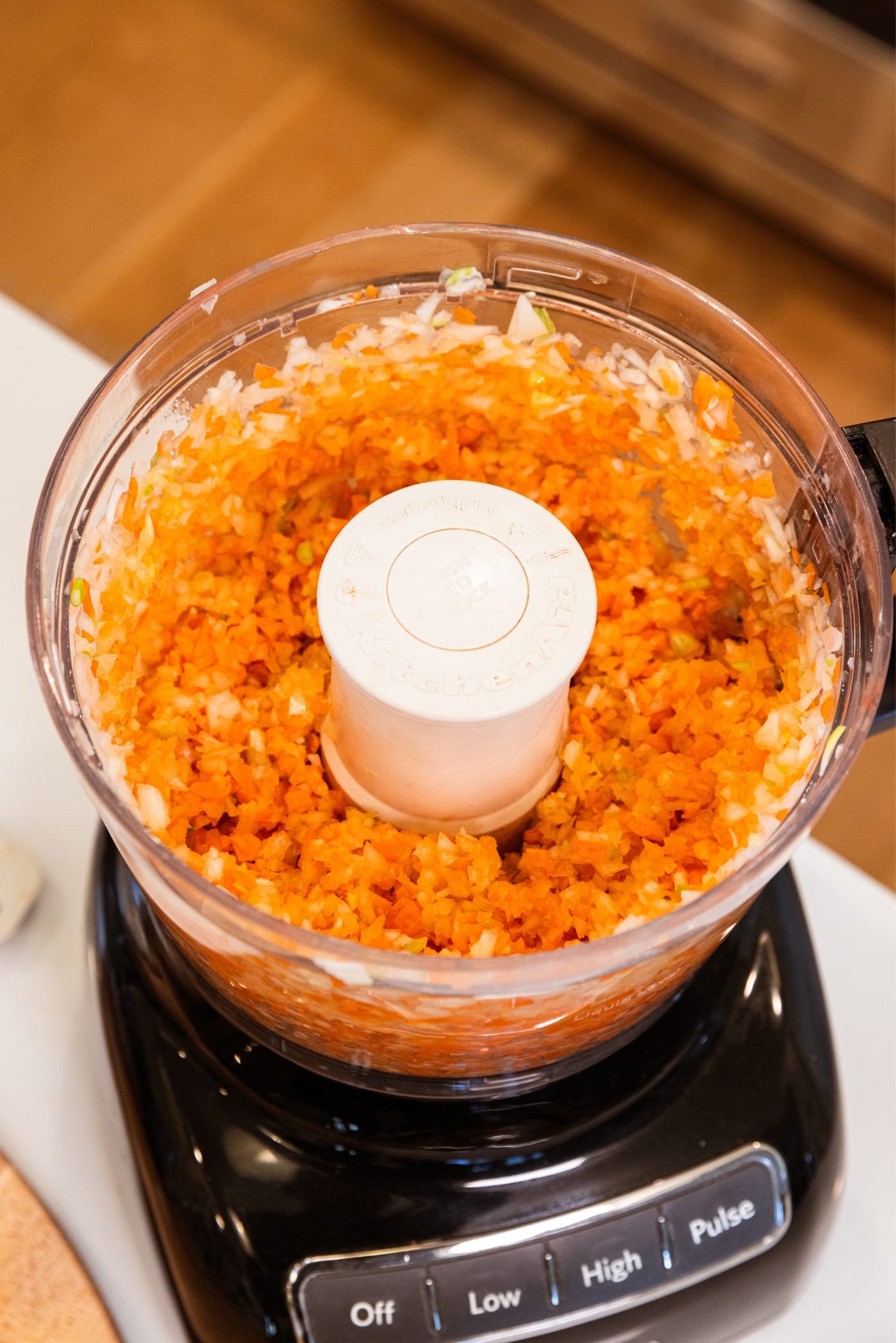 Food processor with finely chopped mixture of carrots, onion, and celery after being mixed together.
