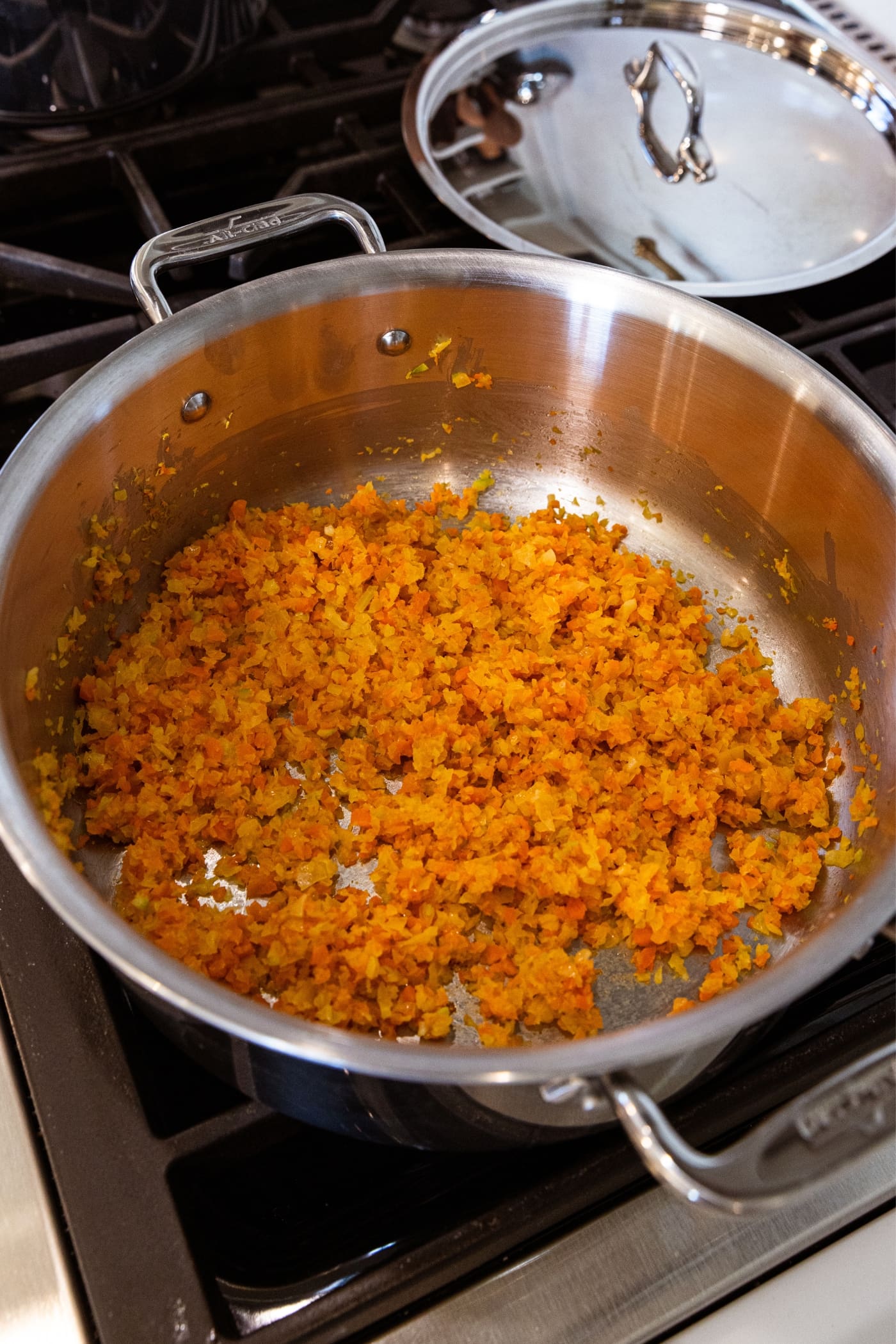 Metal stockpot with cooking carrot, celery, and onion mixture on bottom of pan after cooking in butter for a small amount of time.