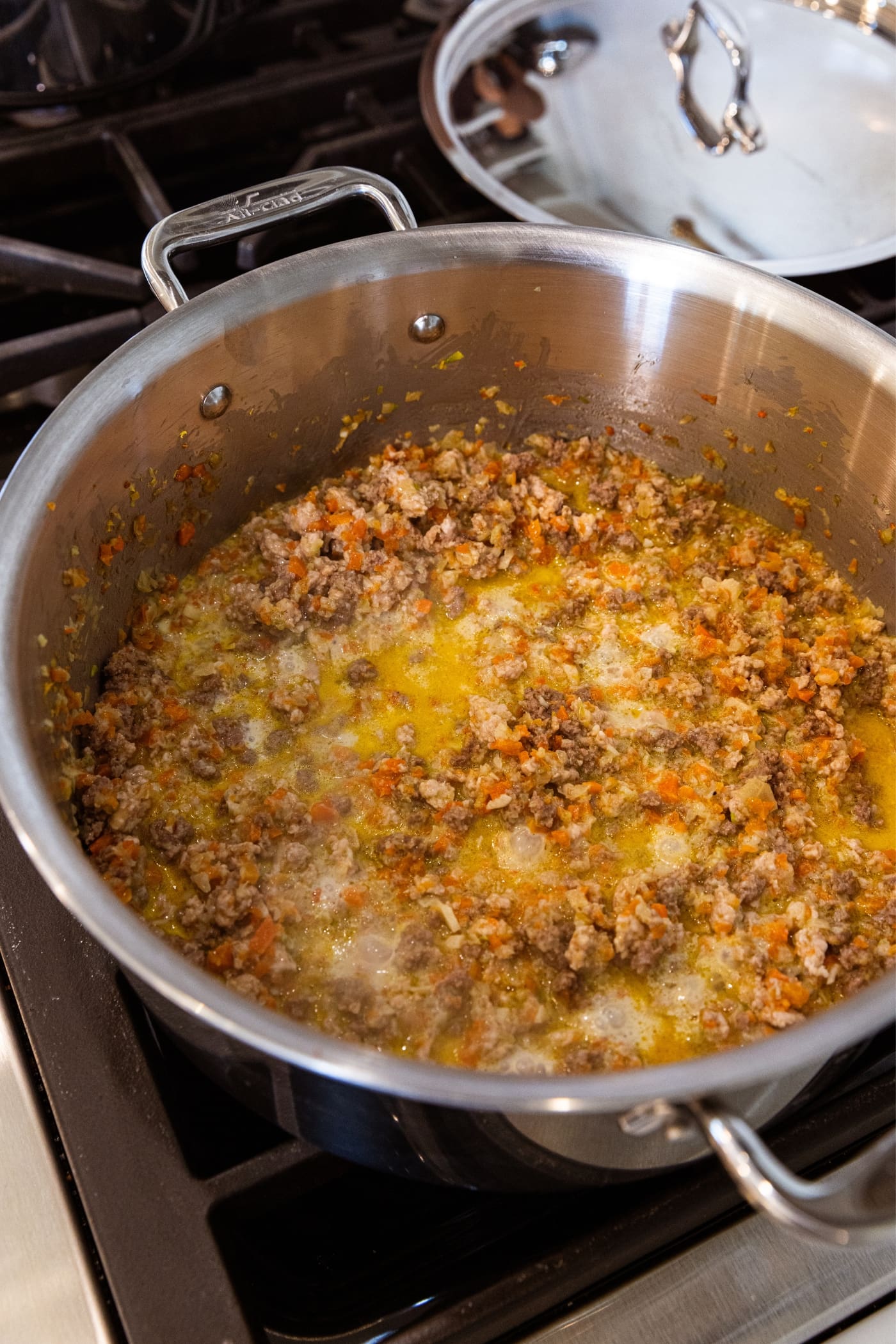 Mixture of milk with meat and vegetables simmering on the stovetop in large metal stockpot.