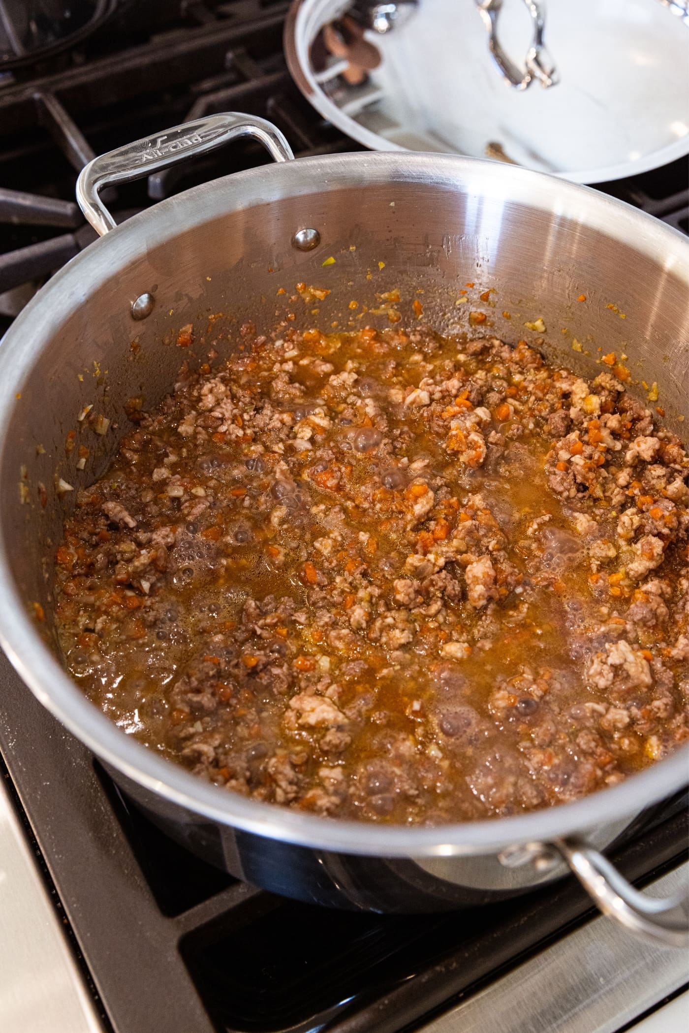Metal stockpot filled with cooking wine and meat and vegetable mixture on the stovetop.