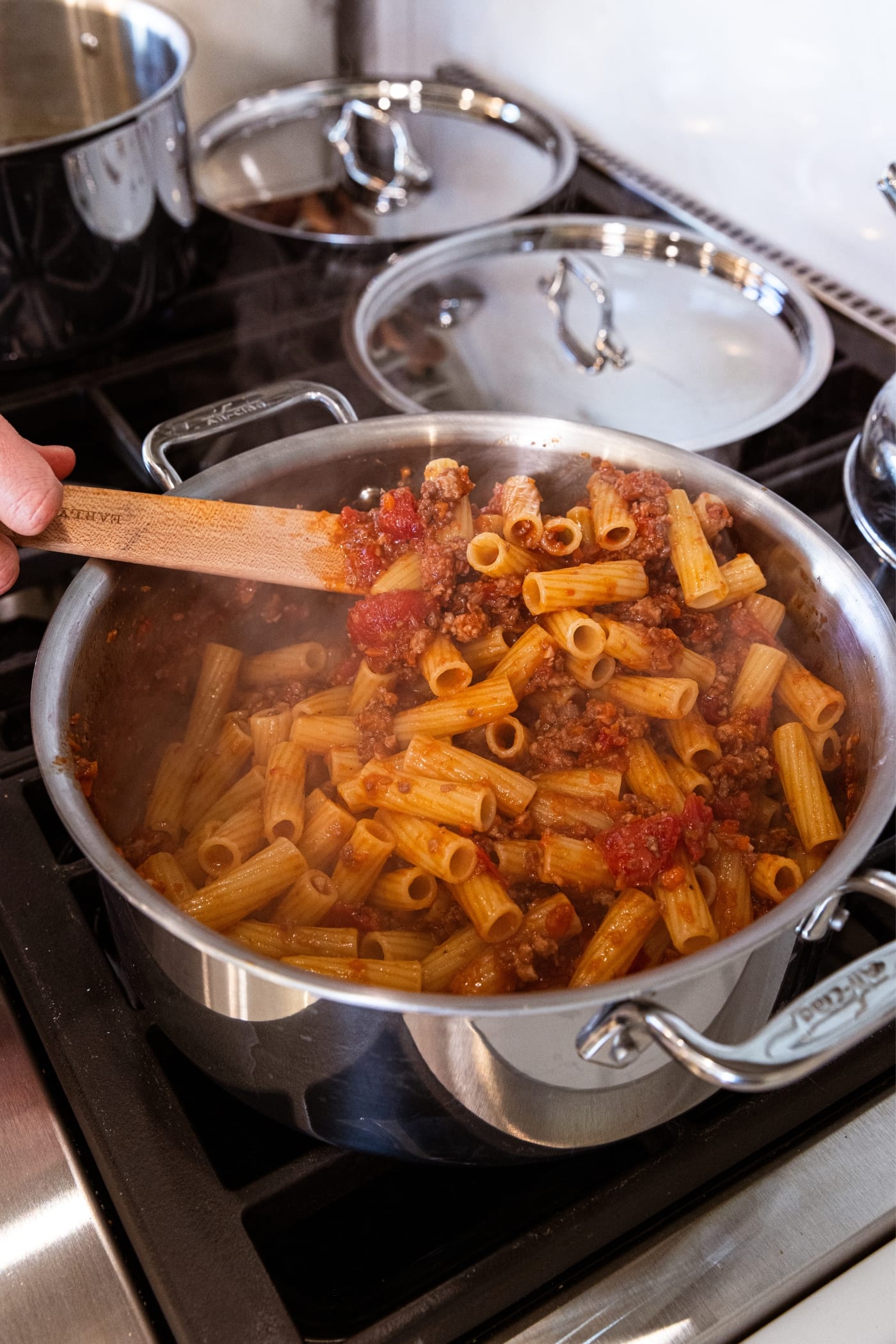 Wooden spoon stirring together pasta with meat sauce in large stockpot on the stove.