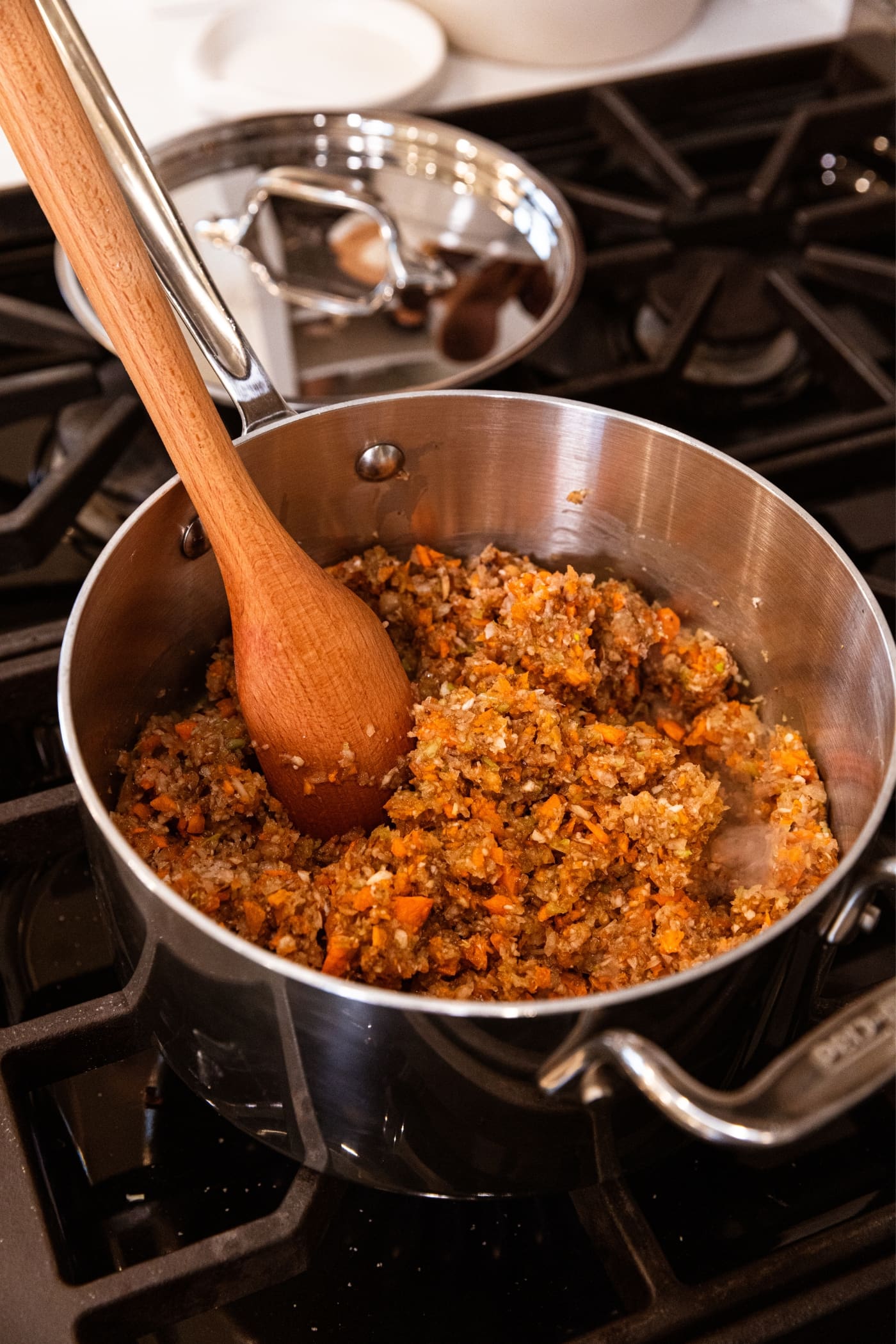 Wooden spoon sitting in metal stockpot filled with tomato paste mixed with vegetable mixture after being ground in food processor.