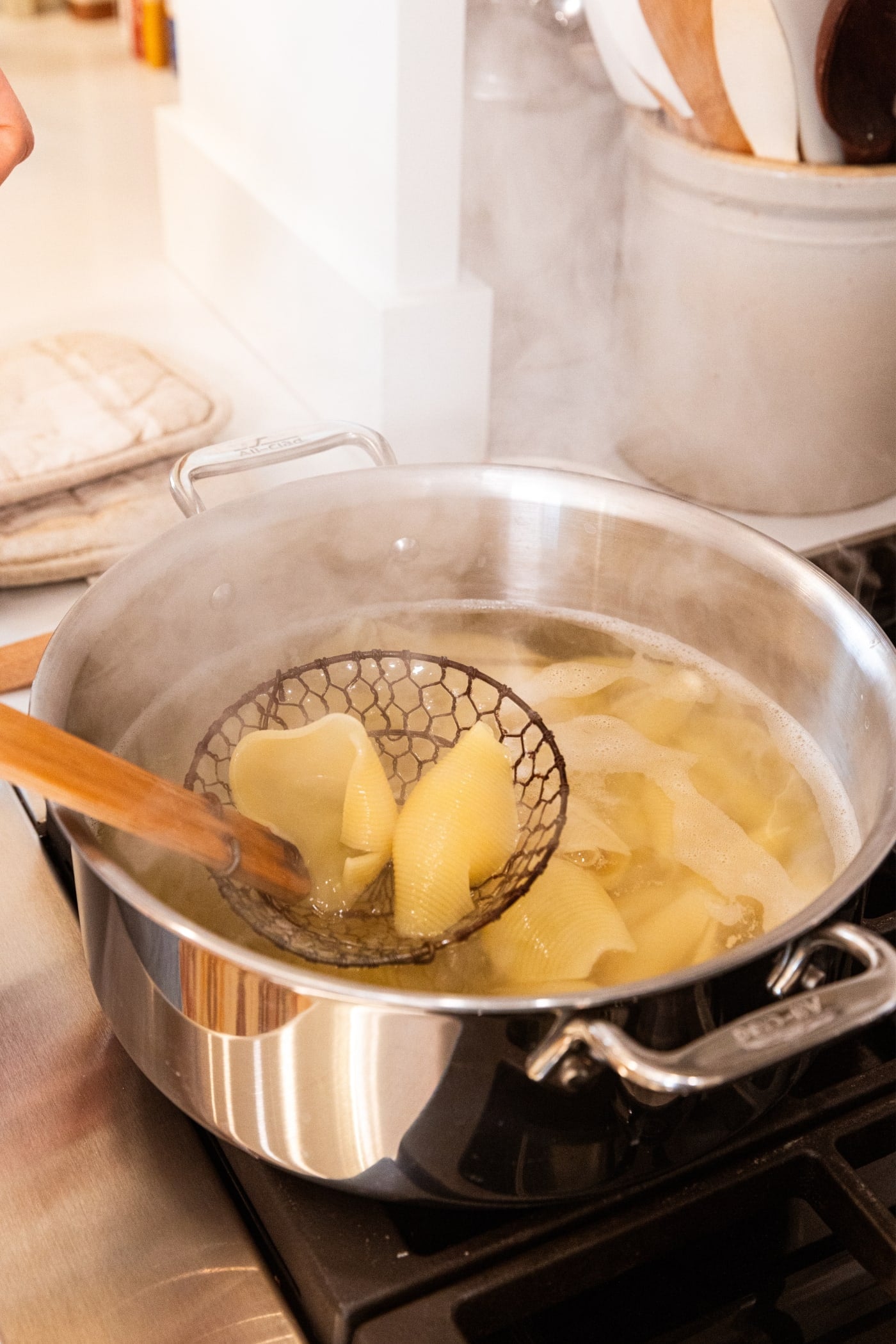 Kitchen spider holding pasta above pasta water in large stockpot after being cooked in hot water.