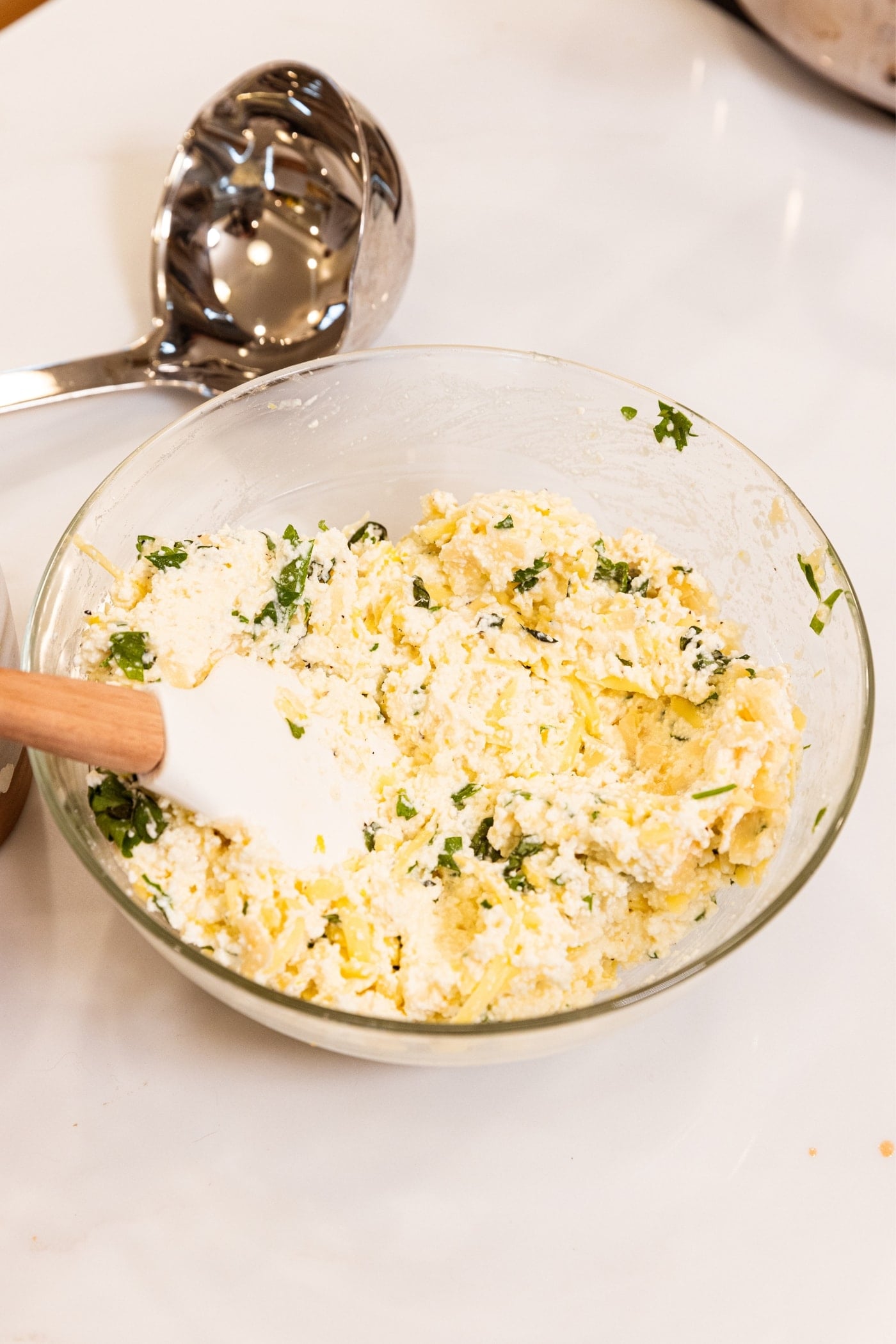 Glass bowl filled with ricotta mixture after being mixed together in bowl sitting on white surface.