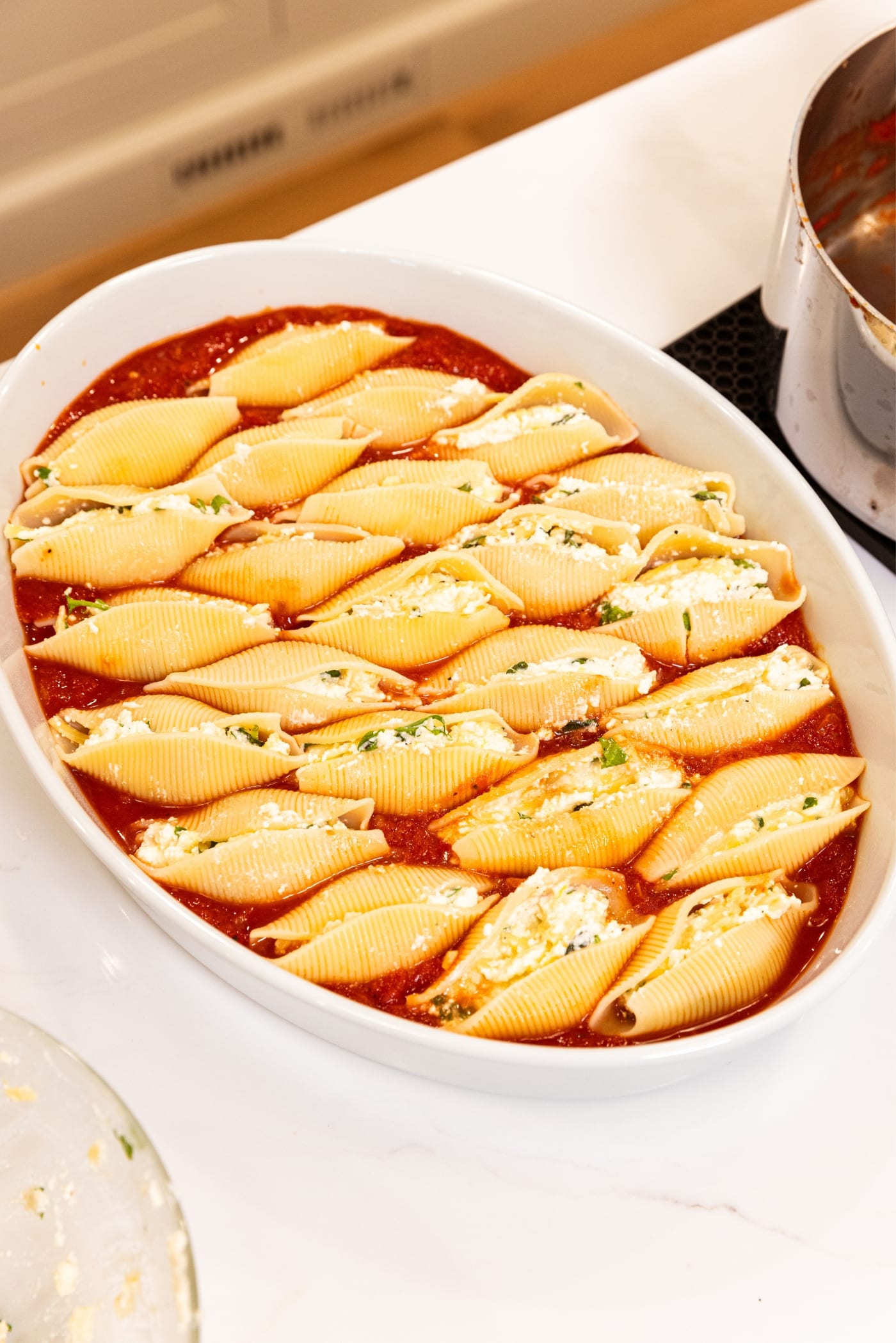 Oval baking dish filled with stuffed shells with ricotta filling inside sitting on top of tomato sauce.