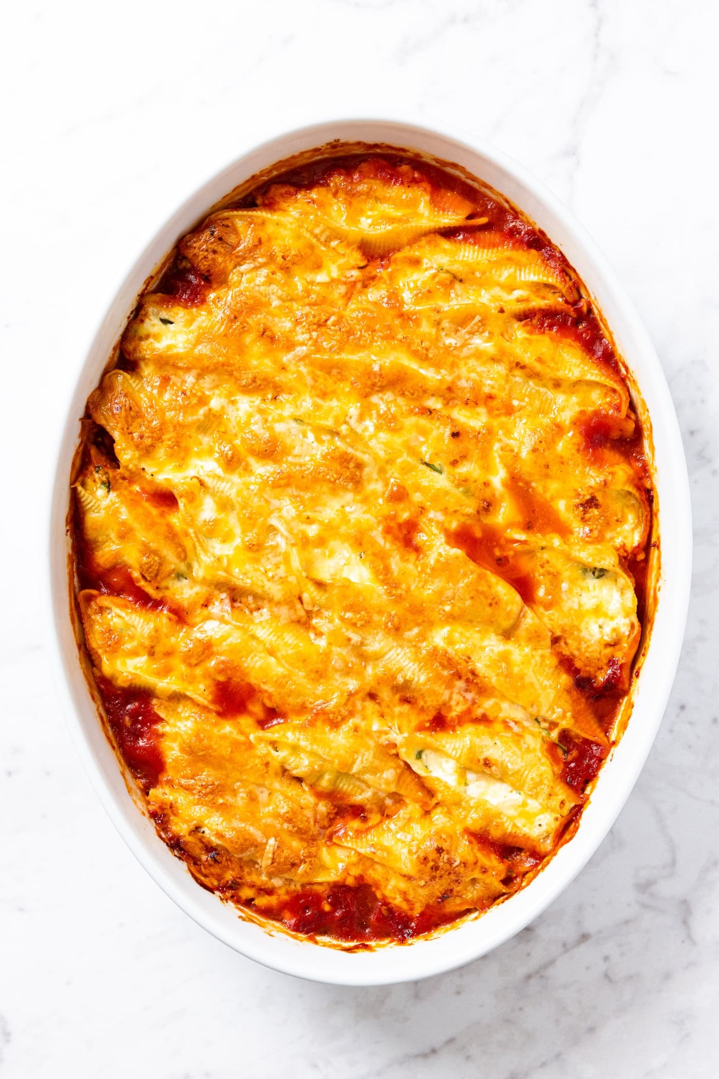 White baking dish filled with stuffed shells with shredded cheese sprinkled all over the top right after coming out of the oven.