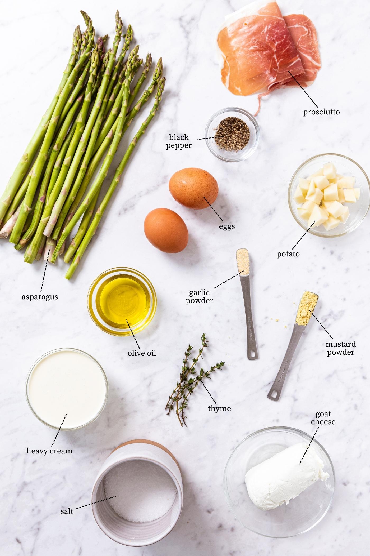 White marble surface filled with all ingredients needed to make a potato frittata including eggs, asparagus, olive oil, cream, spices, herbs, and more.