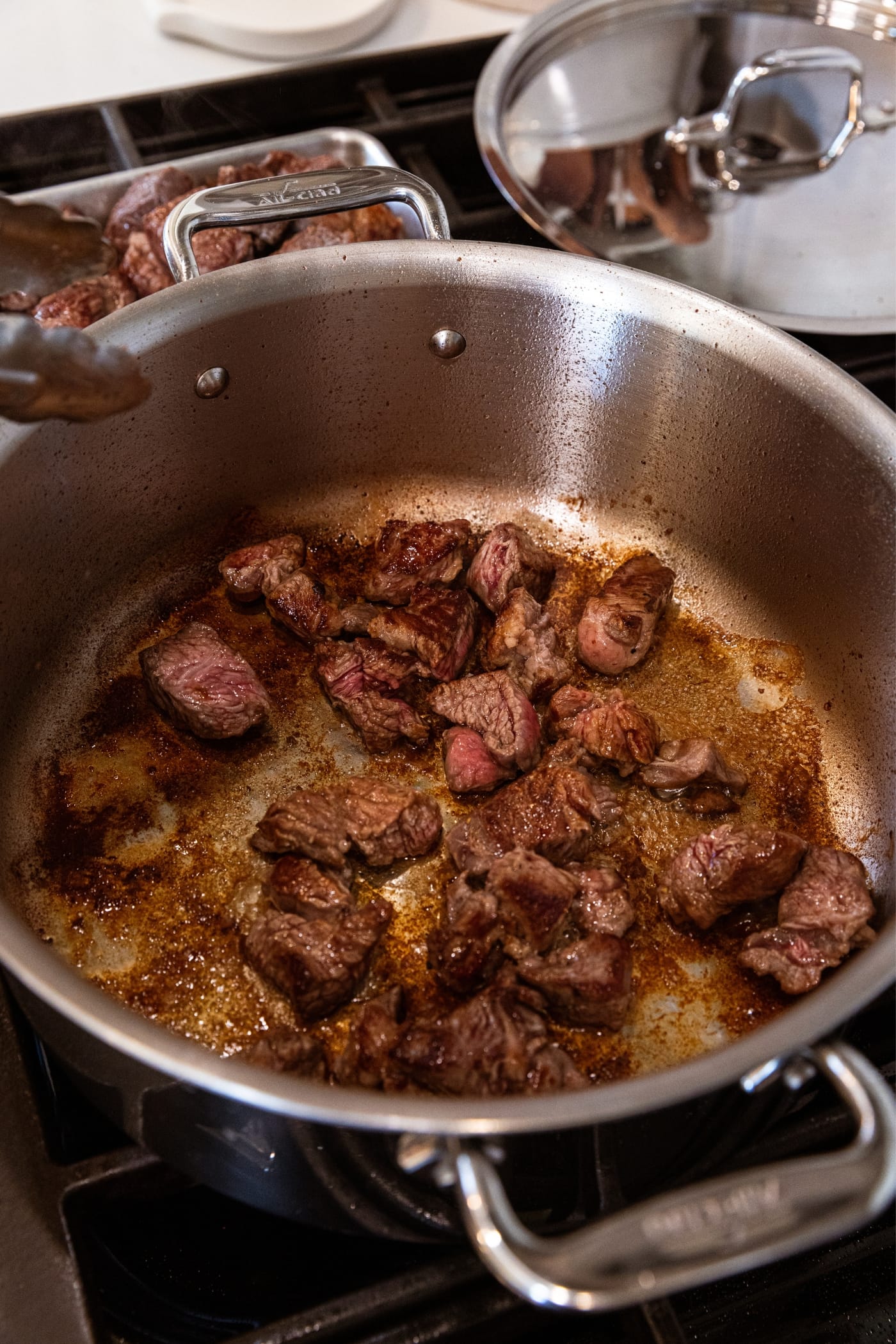 Mostly cooked pieces of chuck roast sitting in the bottom of a large metal stockpot over the heat with browned bits all over the bottom of the pan as well.