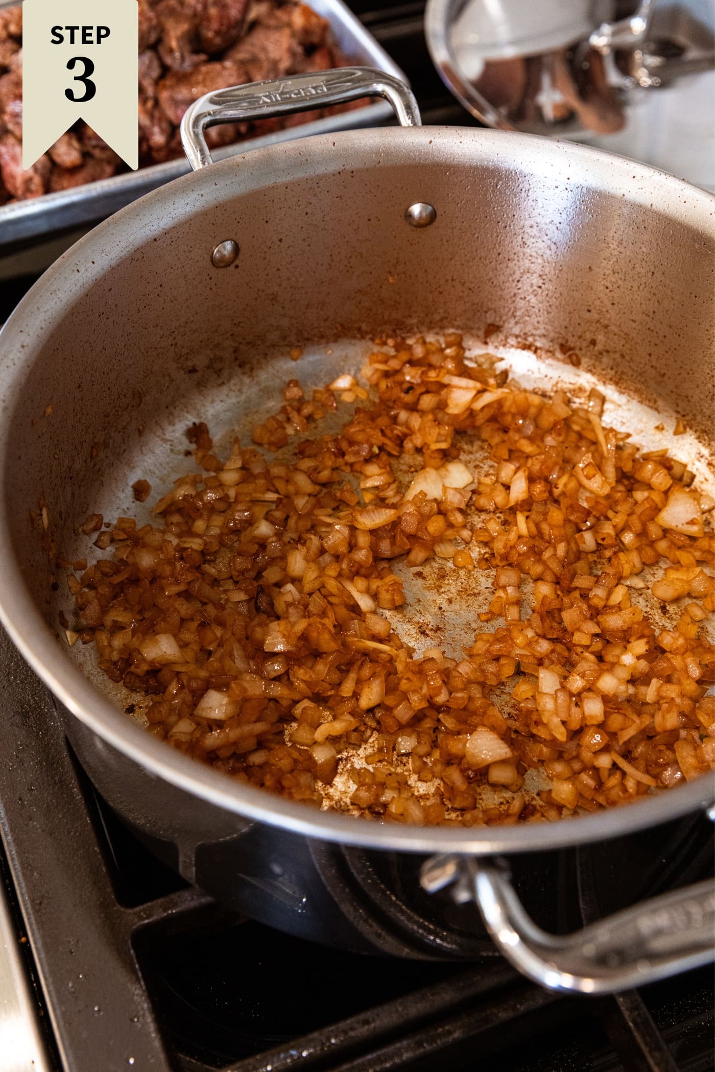 Large metal stockpot sitting on the heat with browned diced onion in the bottom of the pan.