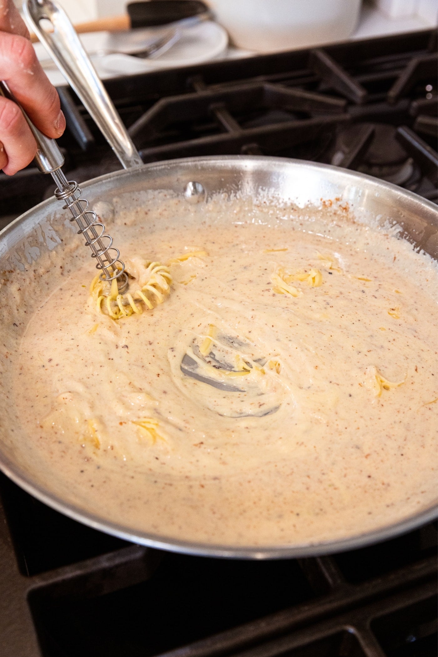 Whisk stirring together cheese into a white sauce in metal skillet on stovetop.
