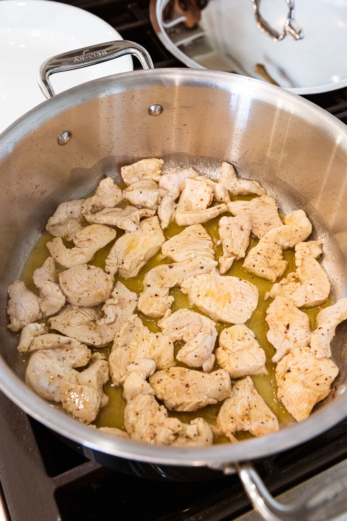 Metal stockpot filled with cooked chicken breast with white skin sitting in butter and oil mixture on stovetop.