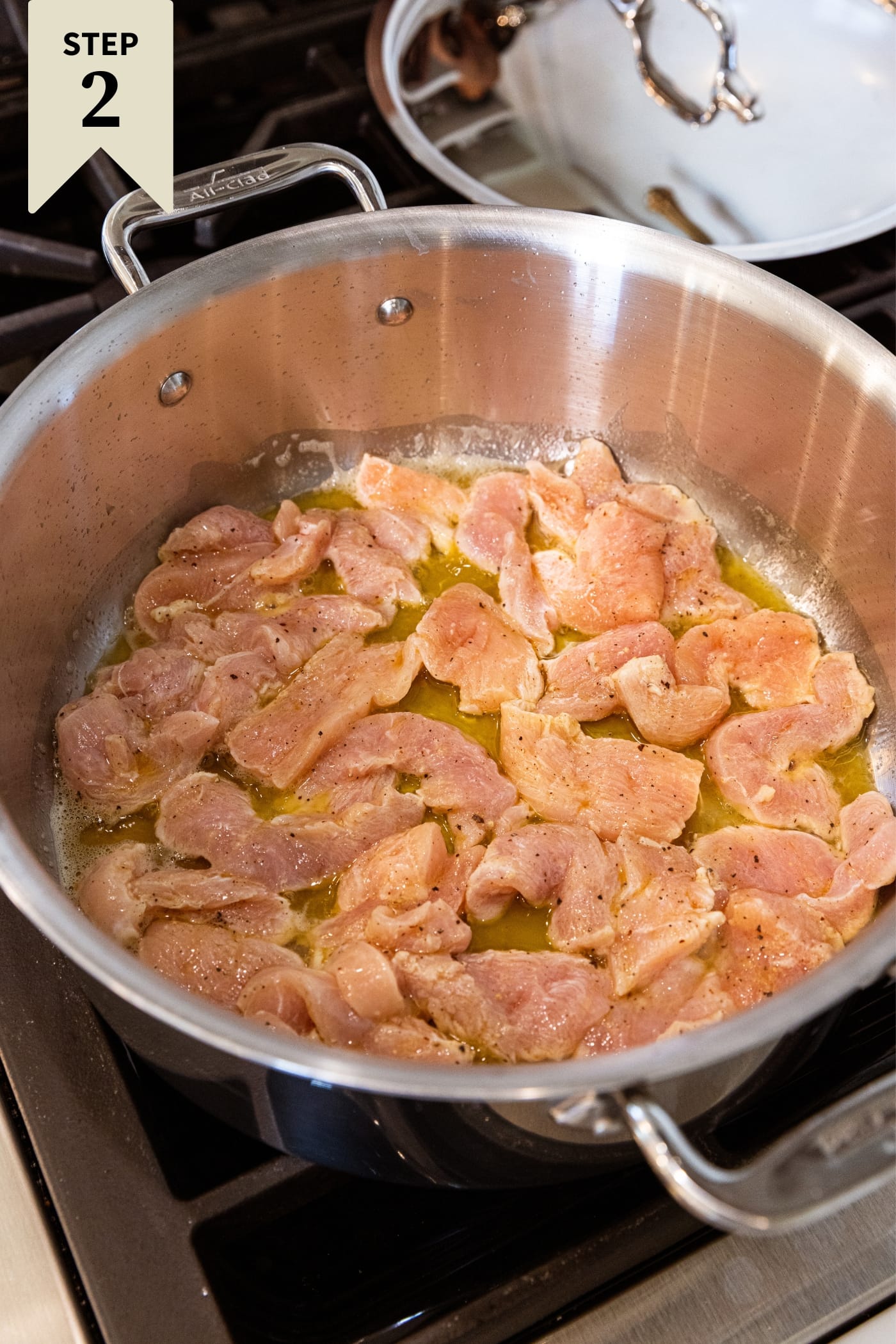 Large metal stockpot filled with raw chicken breast cut into small pieces browning on one side in oil right before being flipped to the other side.