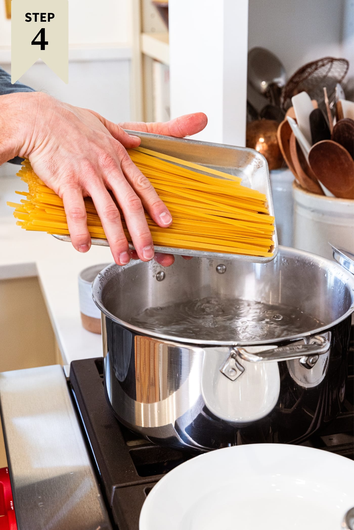 Hands placing uncooked fettuccine noodles into large stockpot filled with boiling water over high heat.