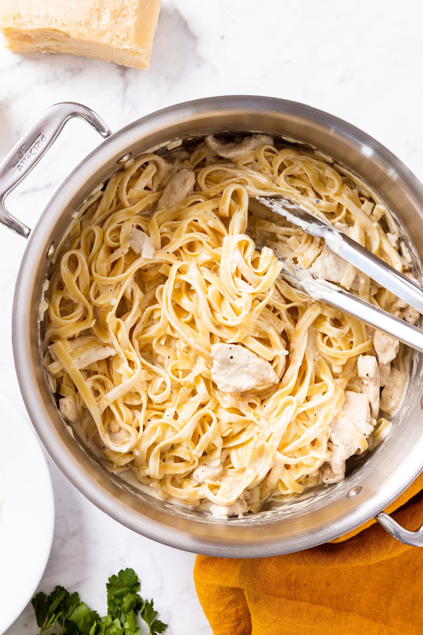 Large metal stockpot filled with cooked fettuccine alfredo with pieces of chicken with tongs twisting noodles together.