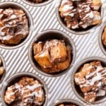 Metal gray muffin pan filled with baked muffins with thin glaze drizzled over the top with one muffin turned on its side to see the interior texture.