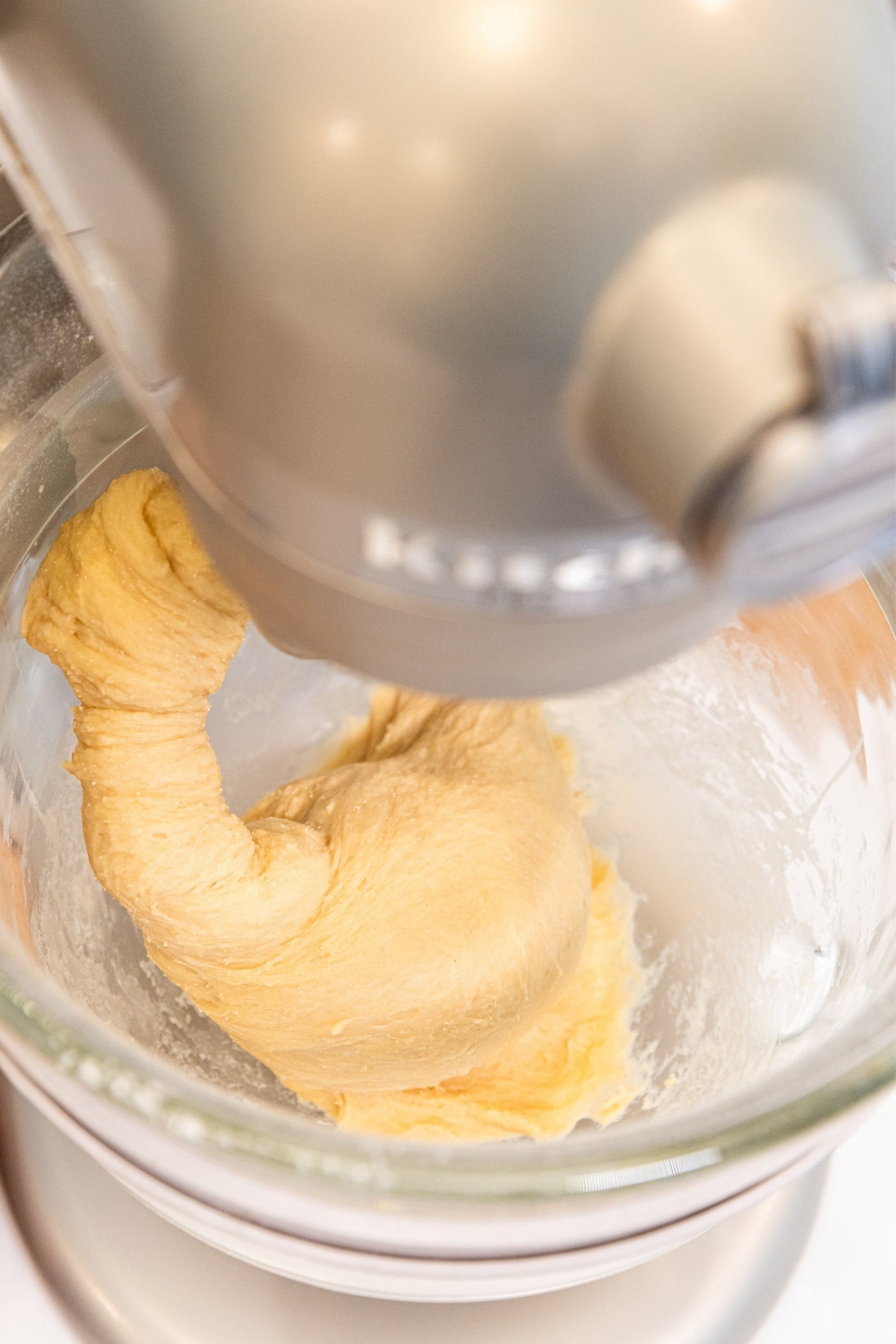 Stand mixer with dough hook attachment mixing together dough that's clinging to the hook.