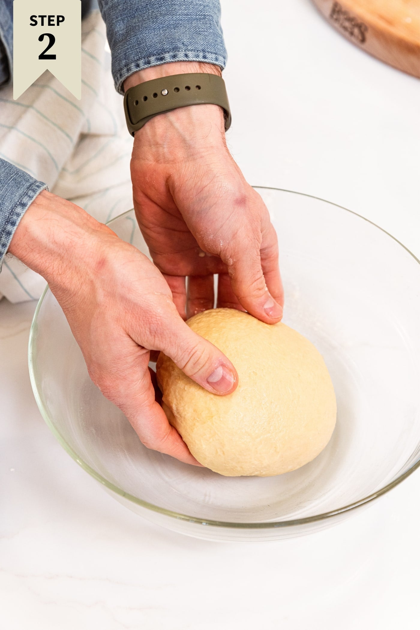 Two hands placing round of dough into a large glass bowl oiled before letting it rise in a warm place.