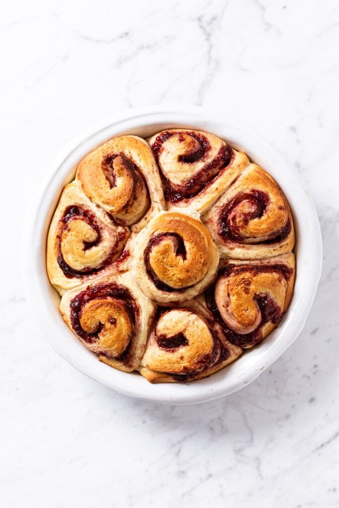 Round baking dish filled with baked raspberry cinnamon rolls with golden brown topping right after coming out of the oven.