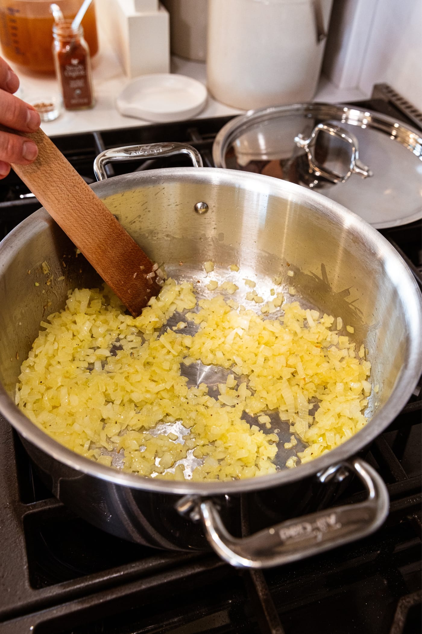 Wooden spatula resting on the bottom of metal stockpot amongst lightly browned onion chopped into small pieces and melted in butter.
