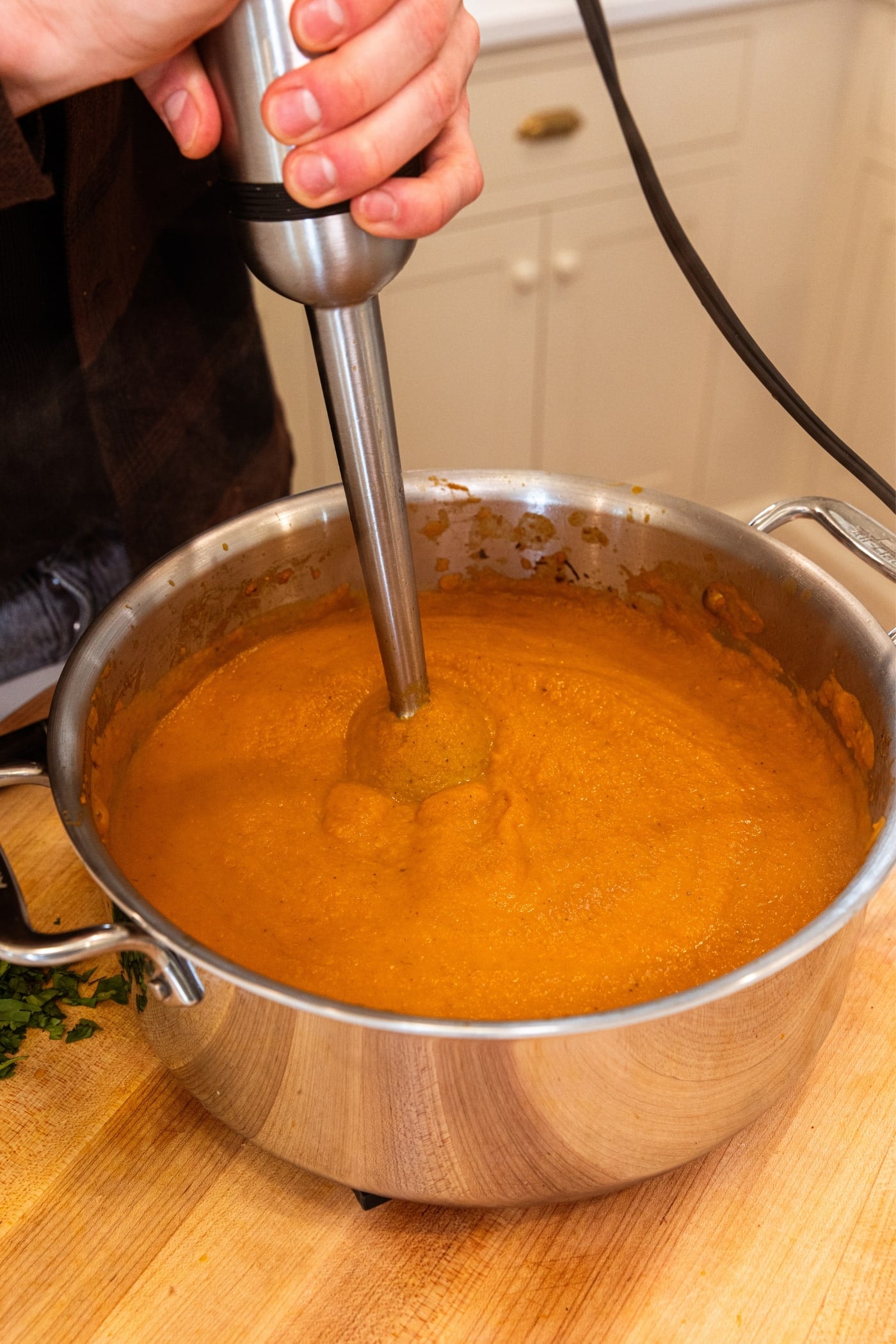 Immersion blender blending together roasted carrot soup until a purée is formed in stockpot.