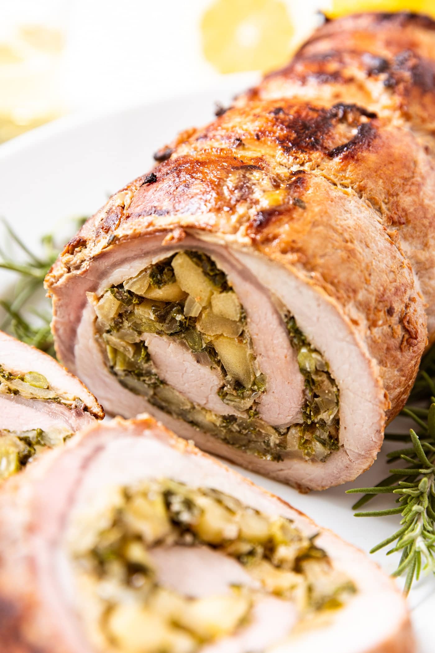 White platter filled with pork roulade with herbs on both sides including two slices off the end showing the interior swirl of the roast including the onion, fennel, and kale filling.