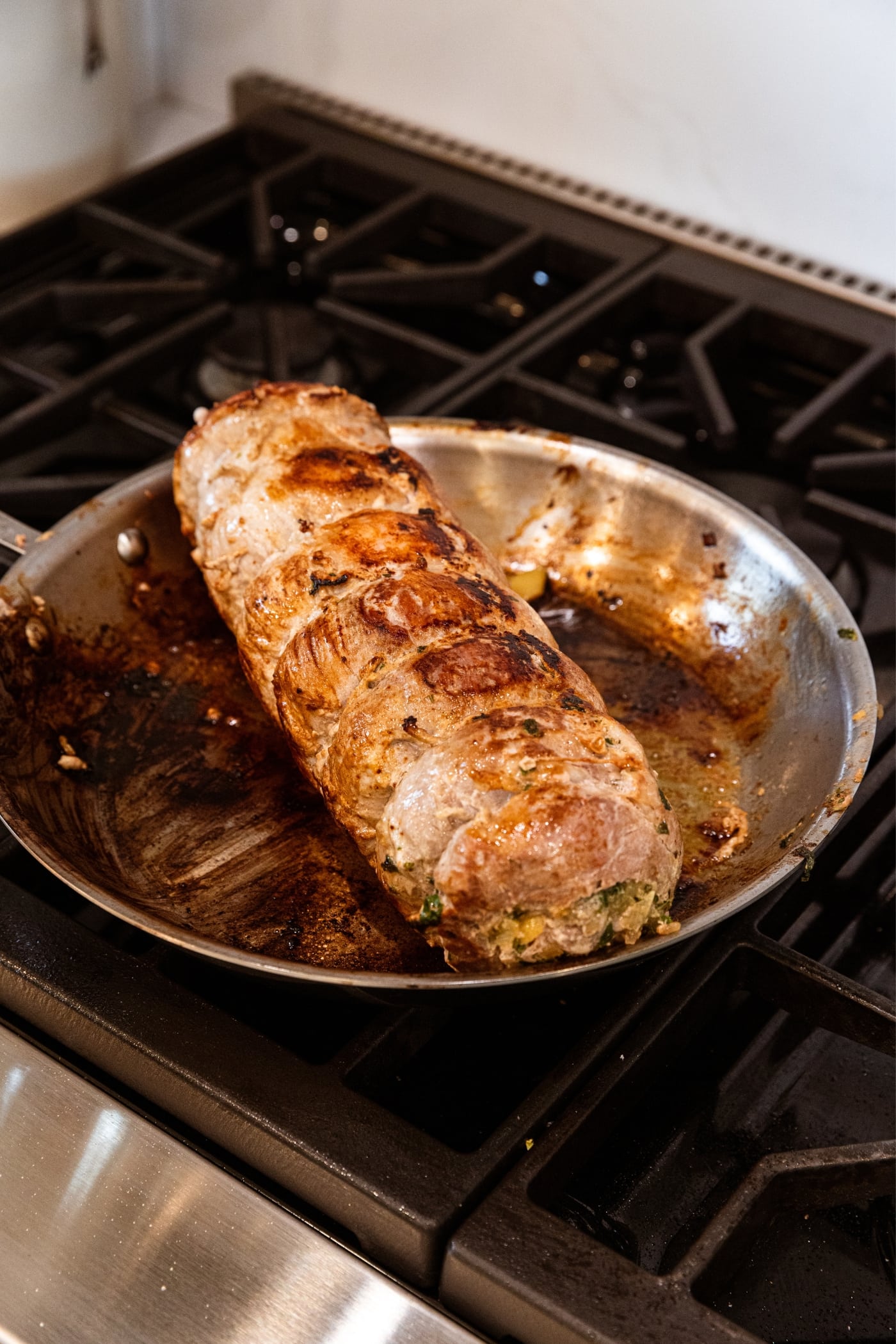 Browned pork roulade with butcher's twine all over sitting in metal skillet on stovetop with browned bits on pan.