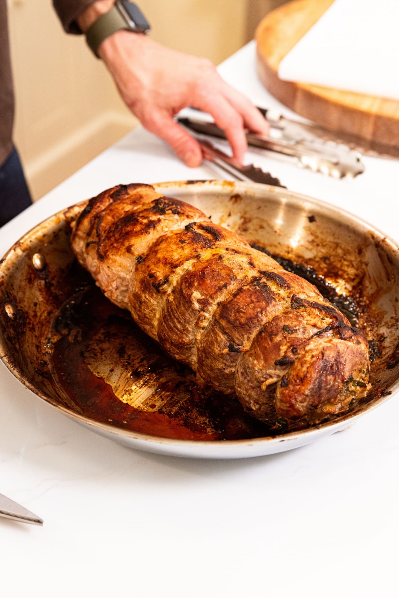 Cooked and browned pork roulade sitting in metal skillet on countertop after coming out of the oven.