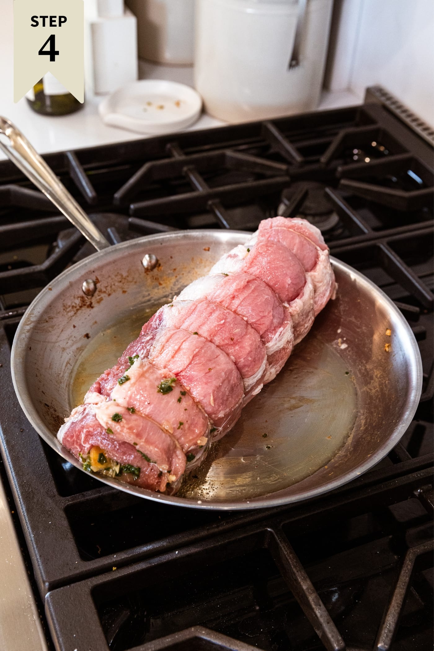 Raw pork roulade with butcher's twine around middle sitting in metal skillet on stovetop right before being browned on all sides.