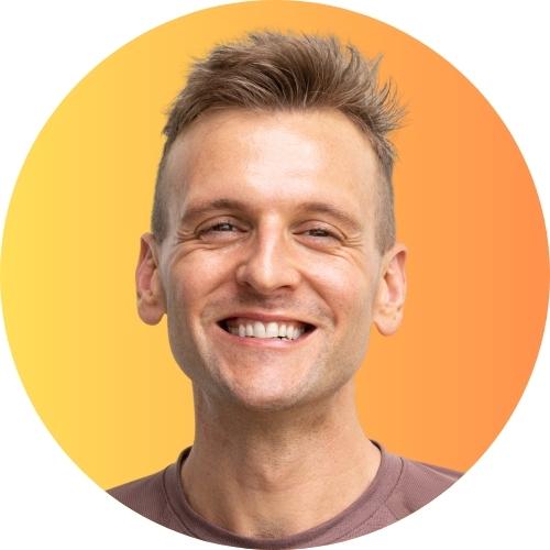 Kaleb Wyse wearing a pink shirt standing in front of yellow and orange gradient background.