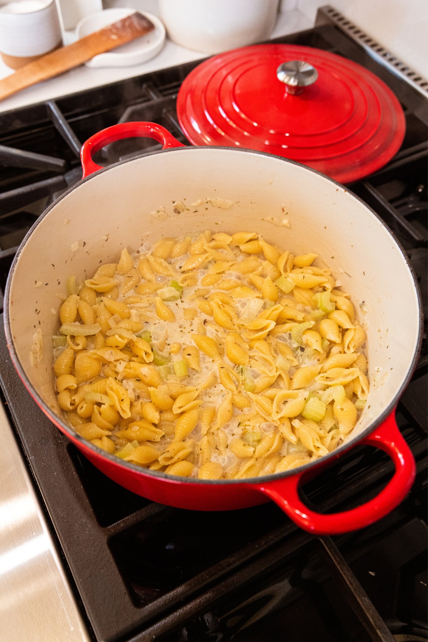 Large red Dutch oven sitting on stovetop with cooking pasta in liquid.