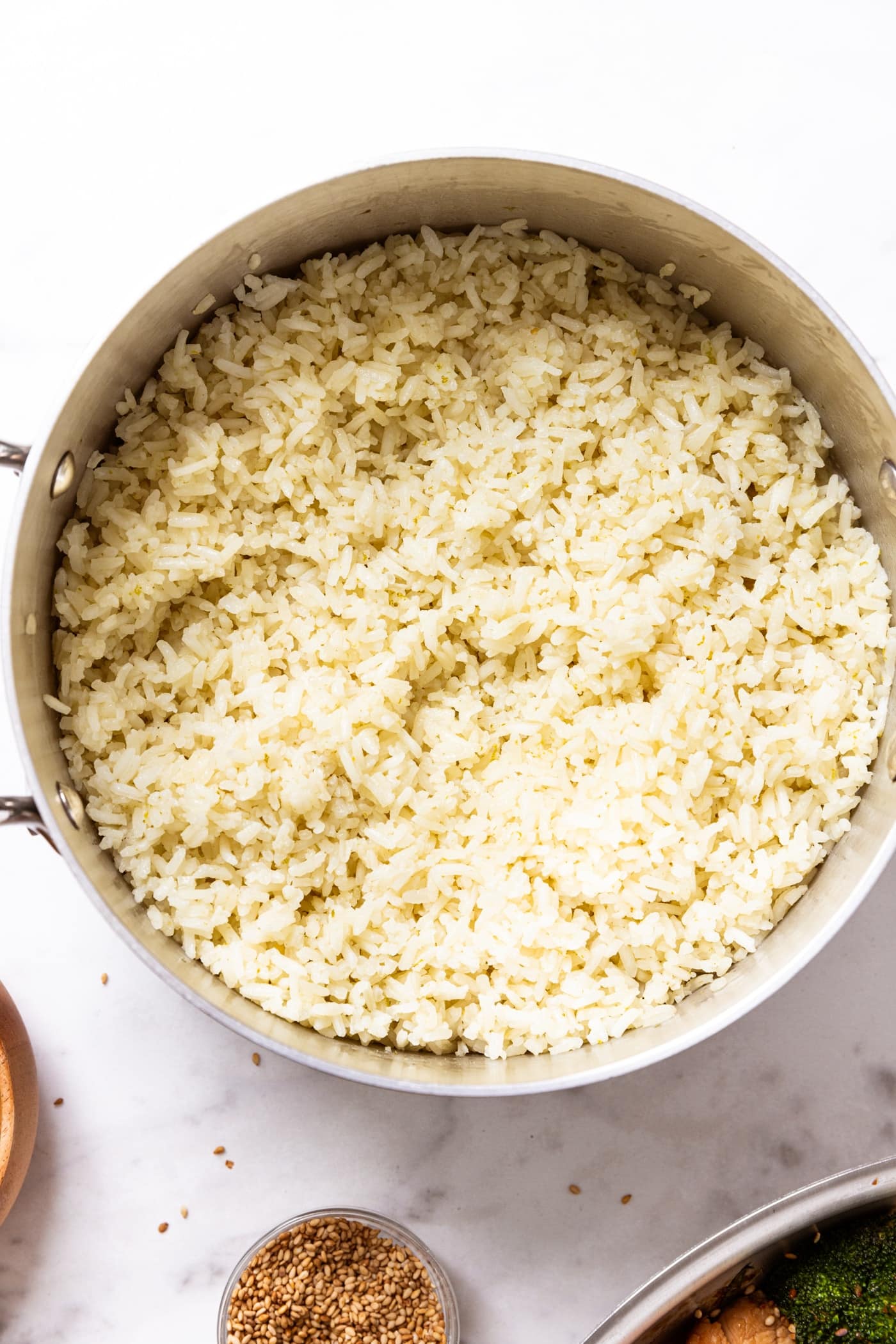 Metal saucepan filled with cooked and fluffed coconut lime rice sitting on white marble surface.
