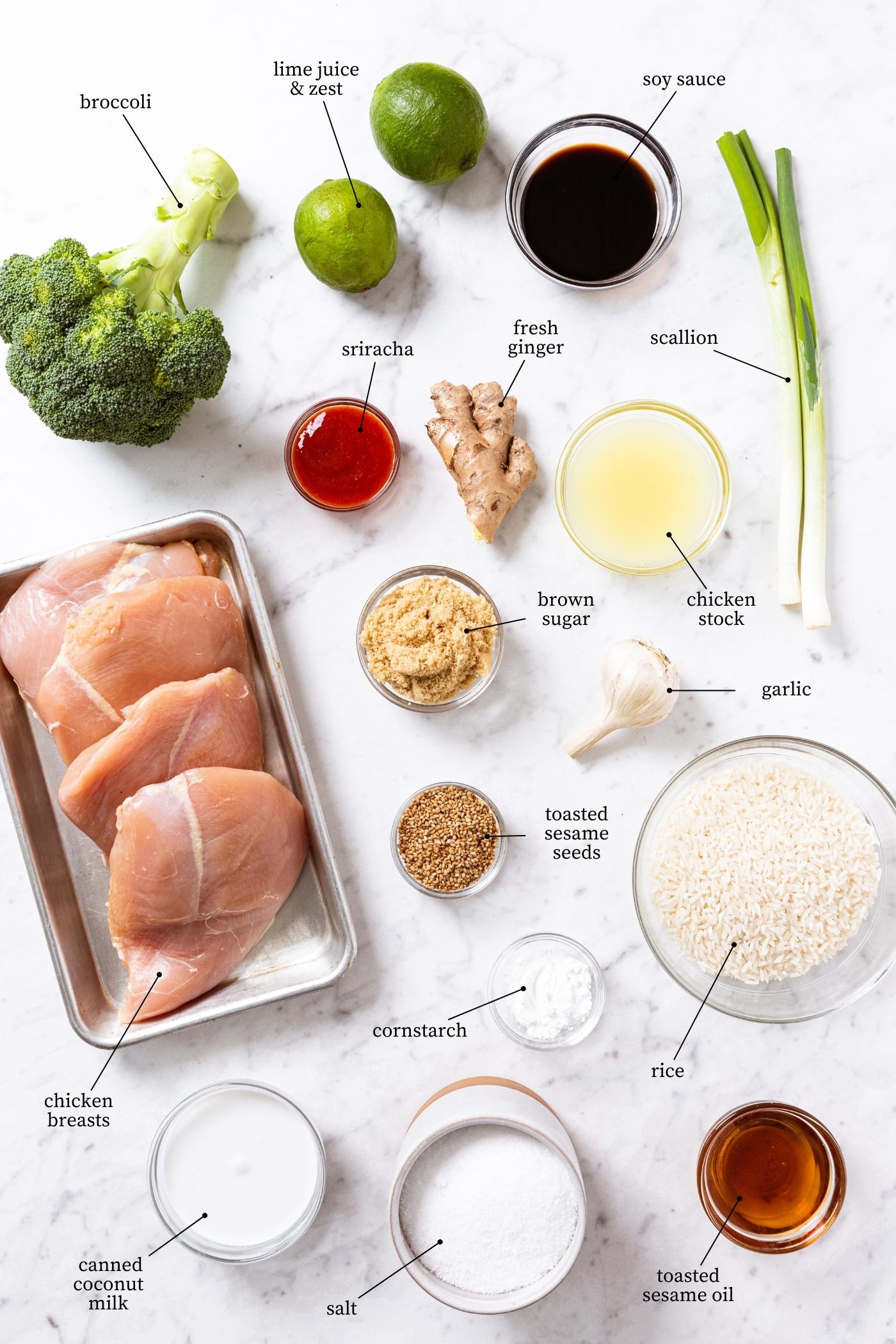 White marble surface filled with all ingredients needed to make sesame chicken with broccoli including chicken breasts, sesame seeds, rice, ginger, sriracha, soy sauce, and more.