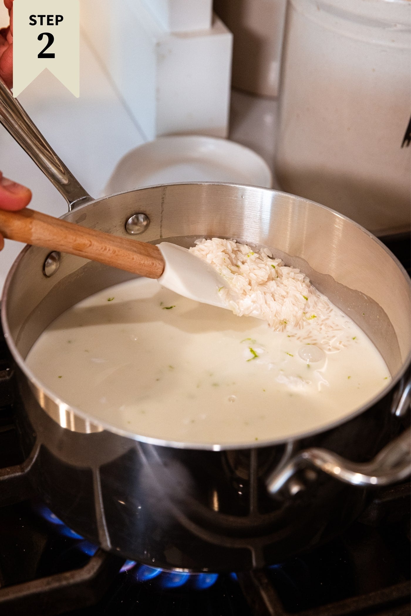 Metal saucepan sitting on stovetop with milk liquid inside with spatula pulling up some of the cooking rice.