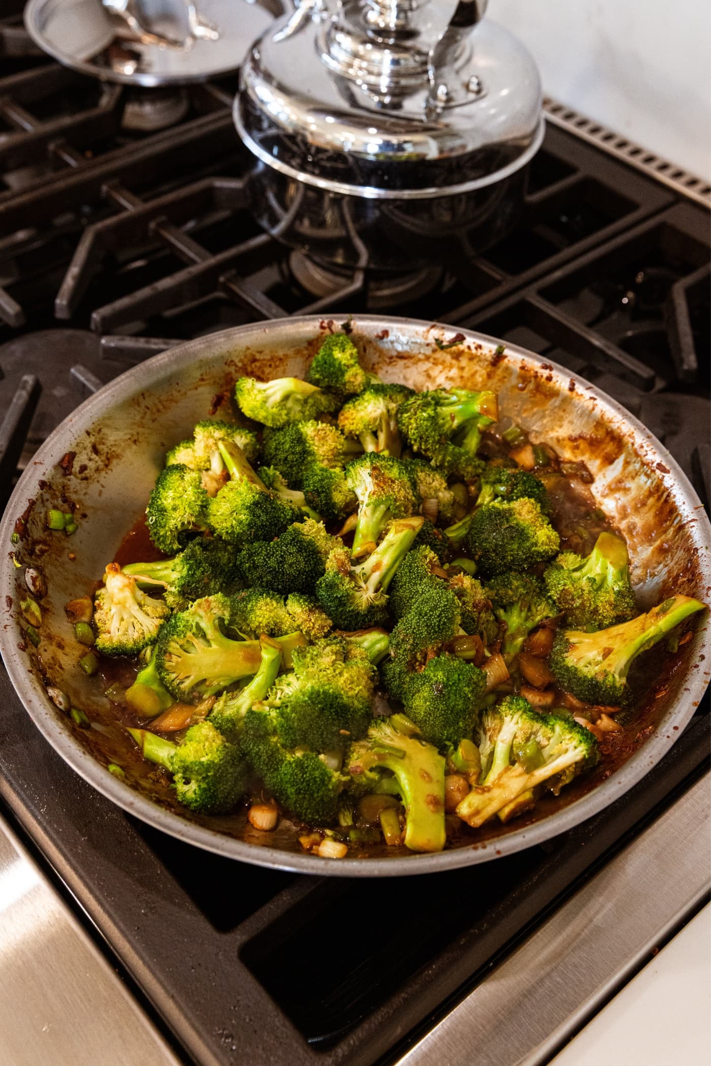 Metal skillet with florets of broccoli cooking in brown soy sauce all on stovetop.