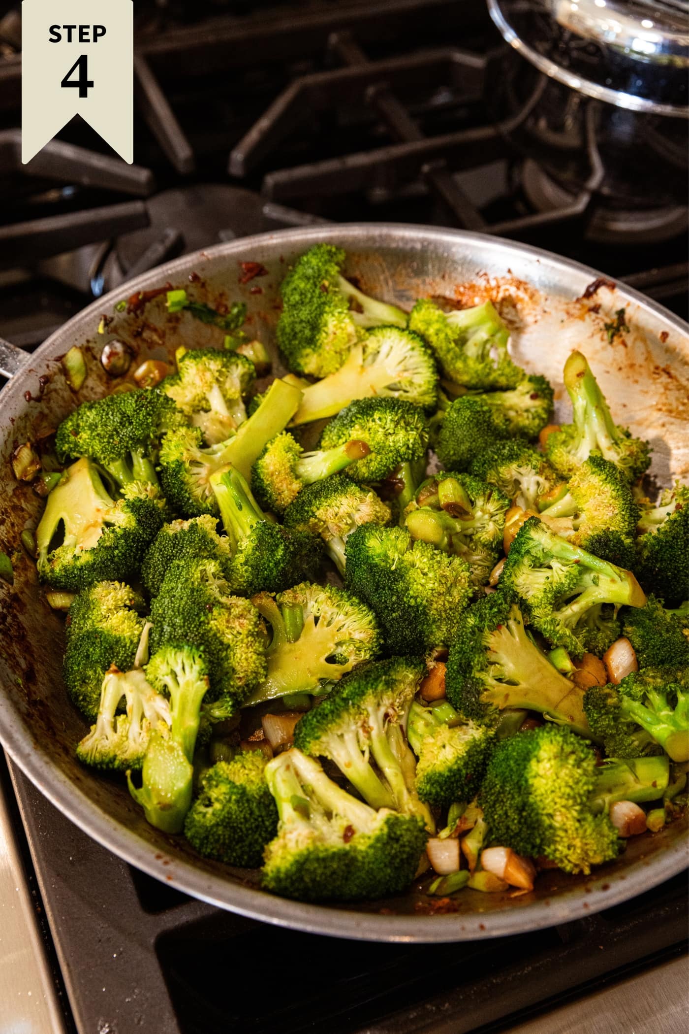 Skillet filled with pieces of chopped broccoli mixing in a sauce and cooking on the heat.