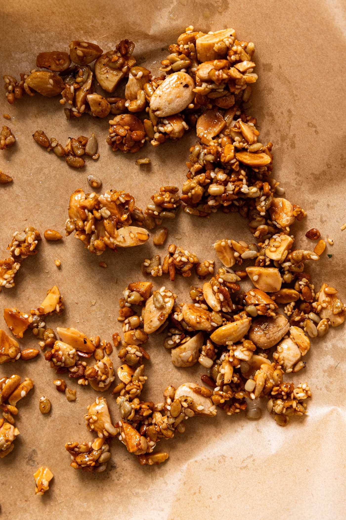 Brown parchment paper sitting on small baking sheet with crunchy nut and seed topping cooling after coming out of the oven.