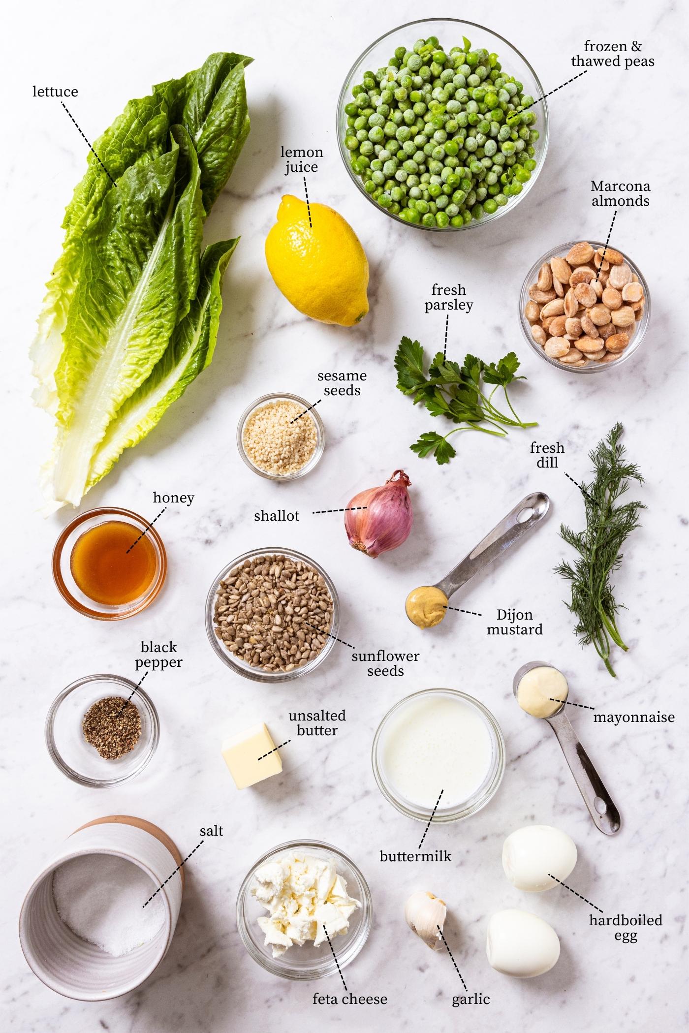 White marble surface filled with all ingredients needed to make a spring pea salad including lettuce, peas, lemon, honey, sunflower seeds, sesame seeds, feta, salt, and more.