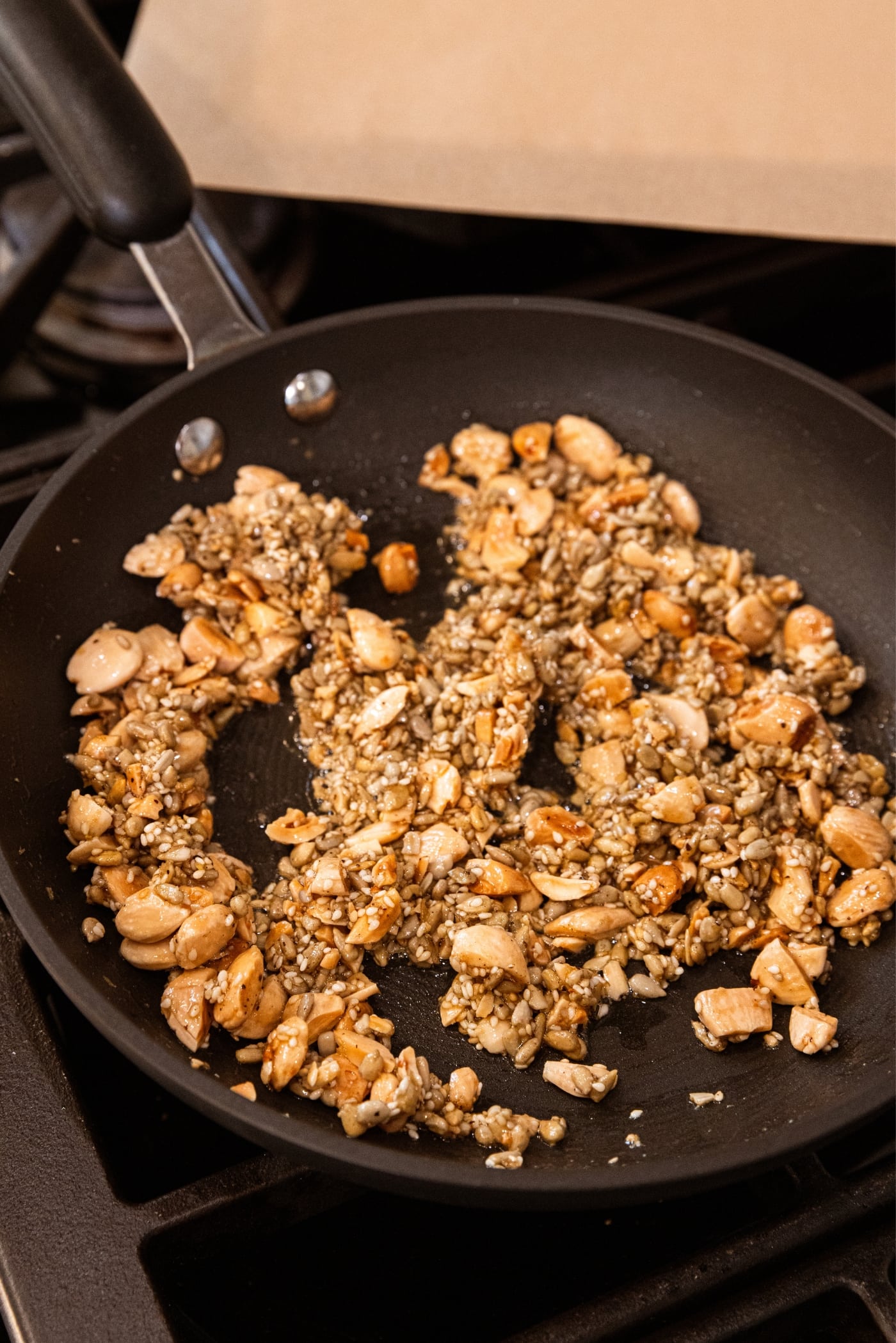 Black skillet with cooked and toasted crunchy nut and seed mixture sitting in clumps.