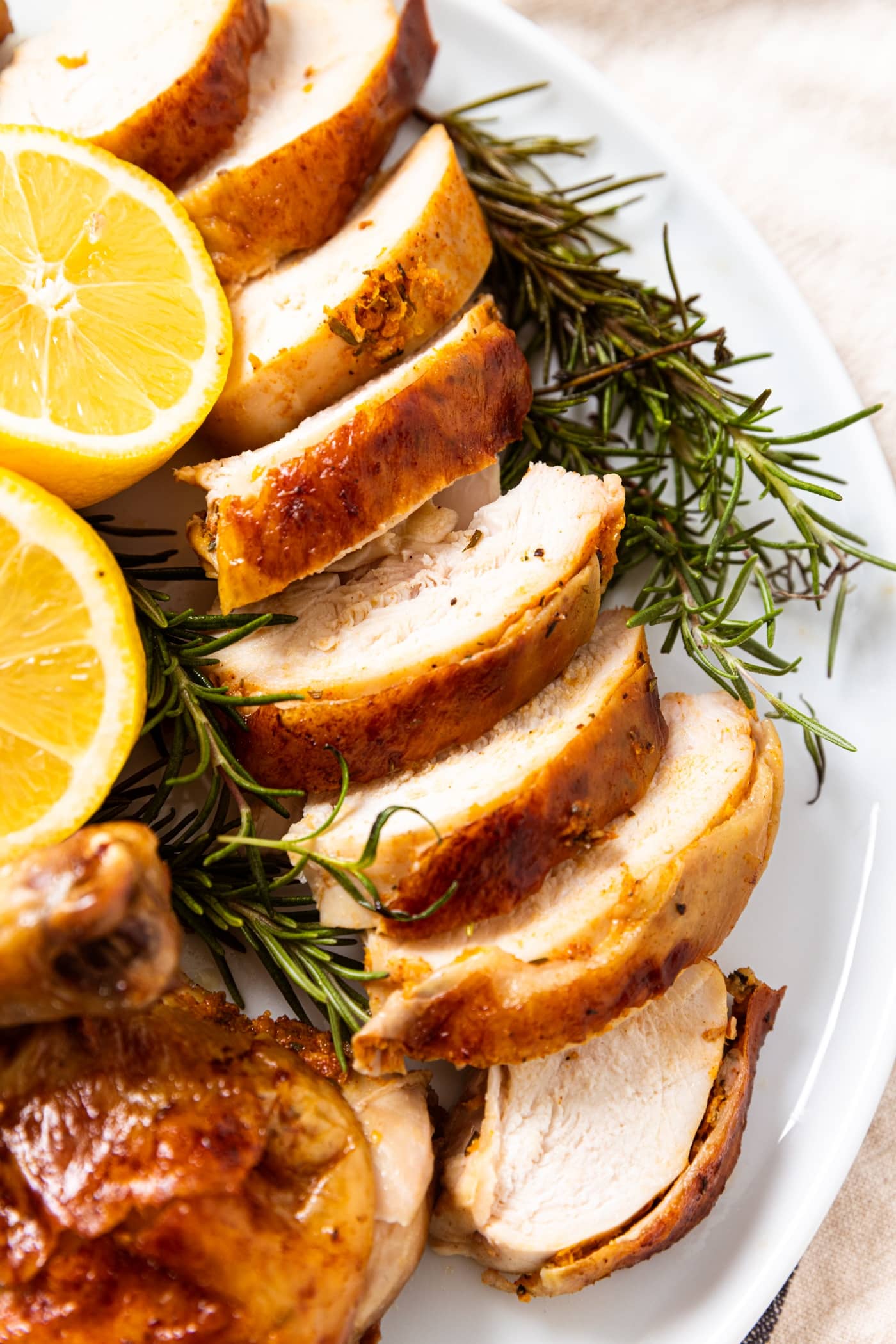 White platter filled with slices of herb roast chicken with slices of citrus and pieces of herbs all around.