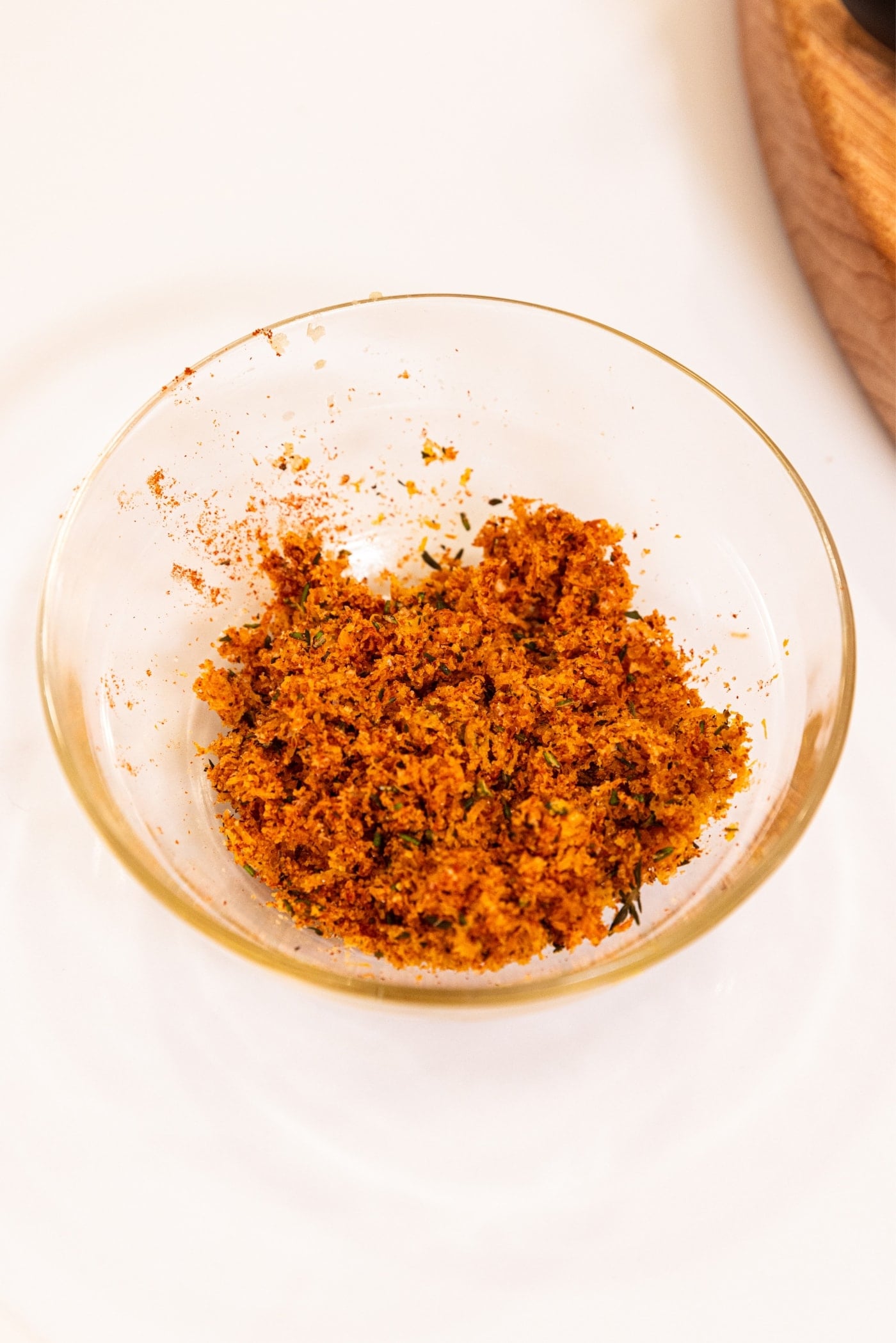 Small glass bowl with mixed spice and salt mixture with brown color all on white countertop with wood cutting board in background.
