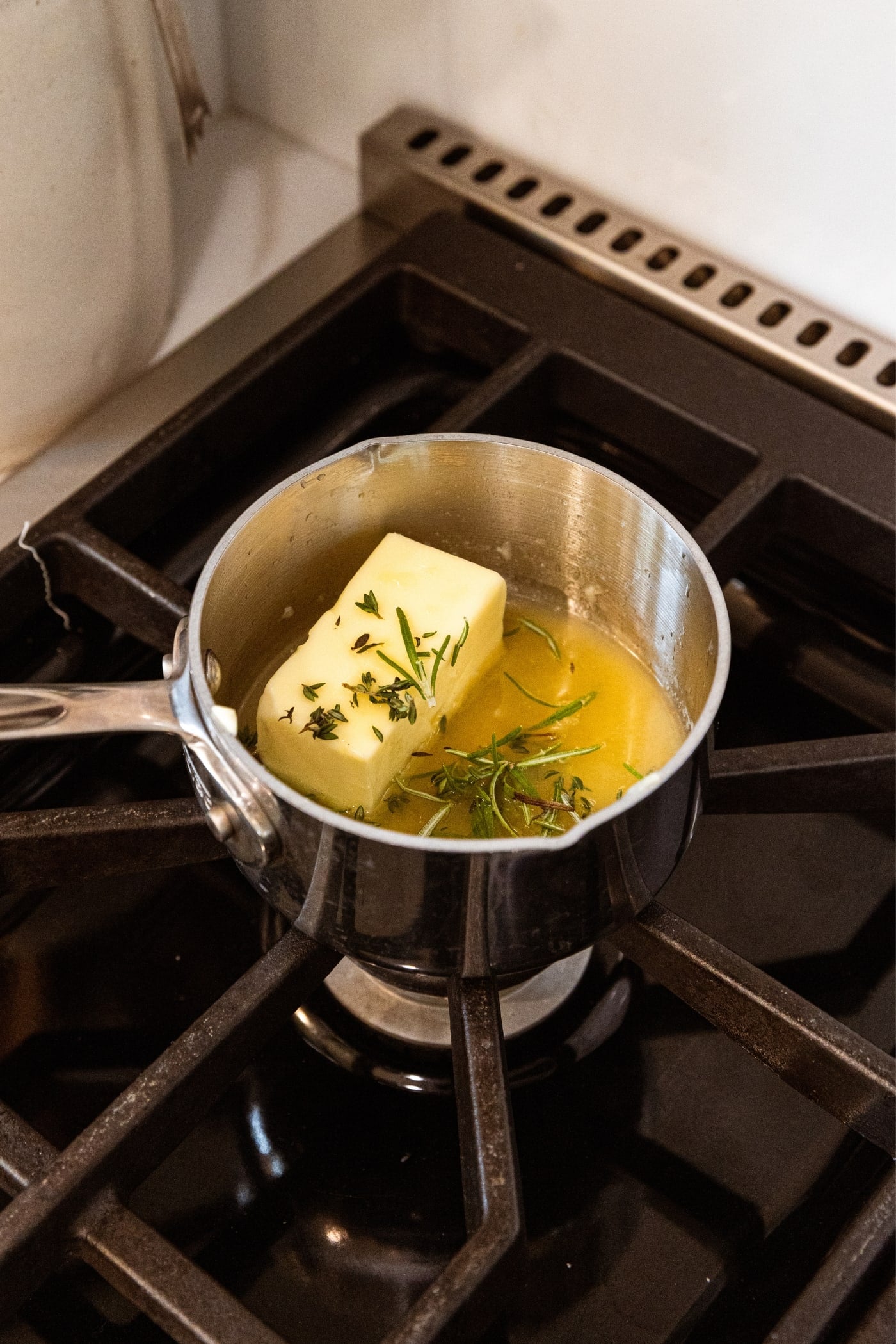 Small saucepan sitting over heat with unmelted butter and combination of herbs before melting fully.