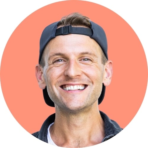 Pink background with man standing in front wearing black shirt and black backwards hat.