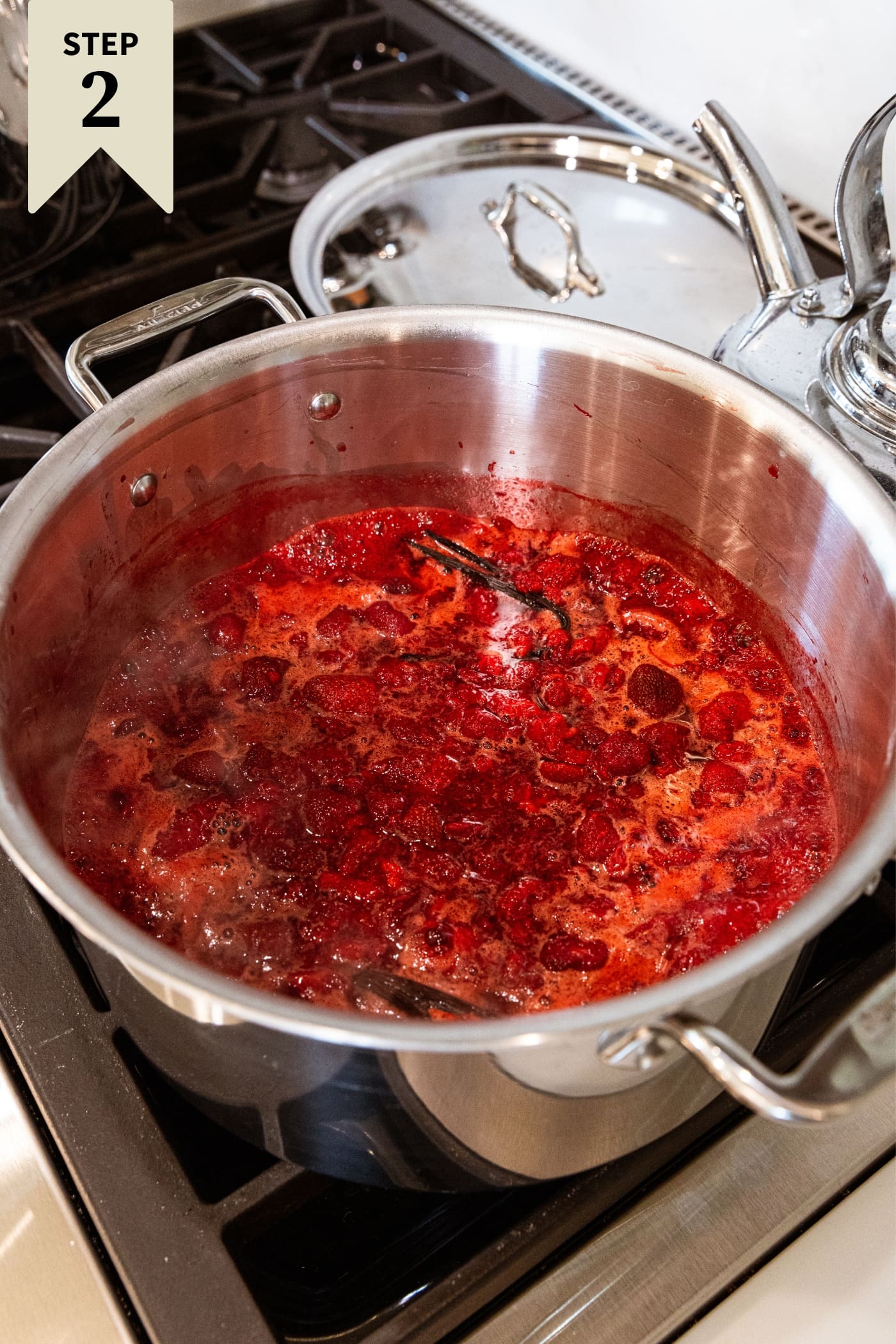 Large metal stockpot with mashed and cooked strawberry and sugar mixture heating with foam resting on top.