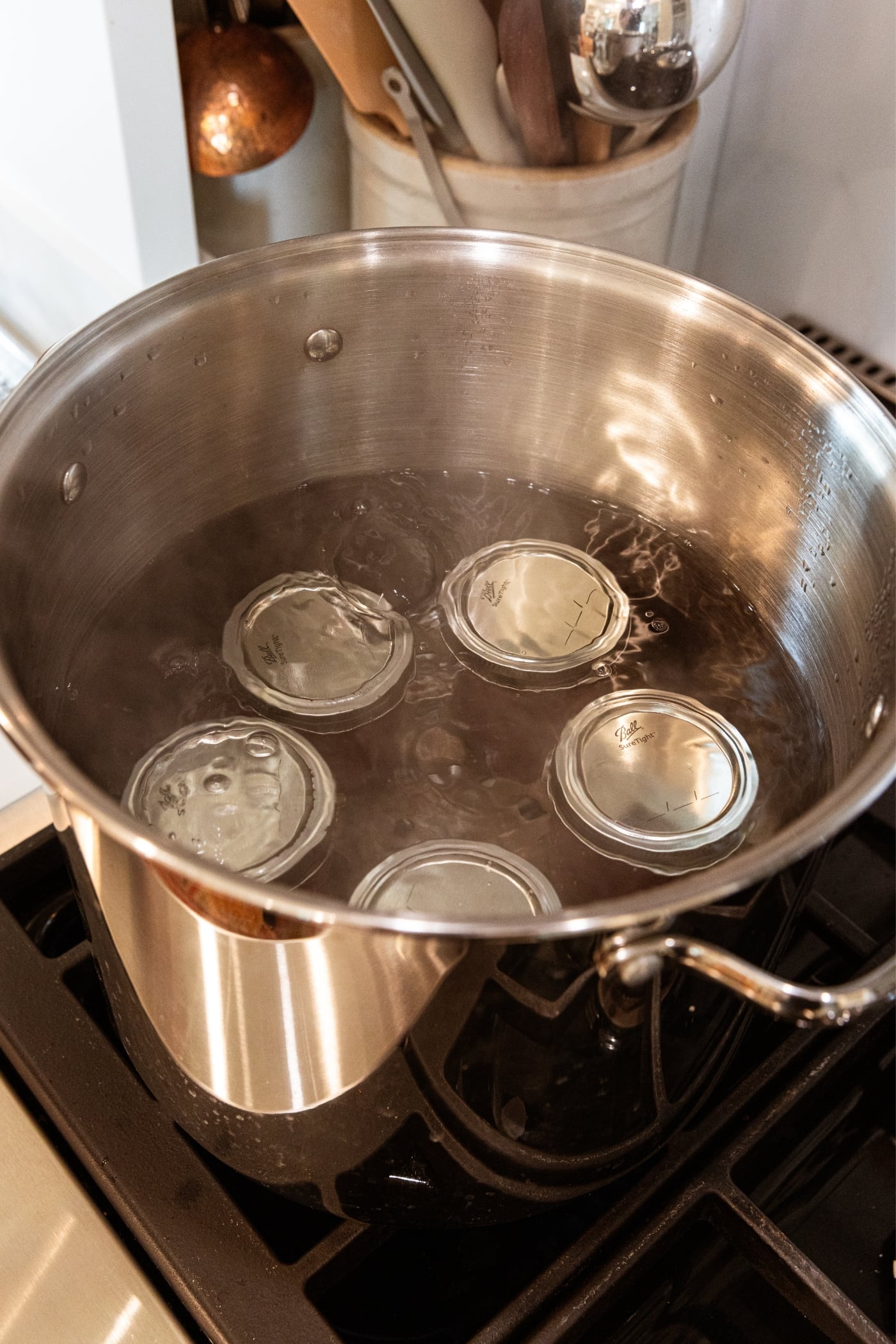 Large metal pot filled with jam jars with metal lids and rings with water covering the jars all on stovetop.